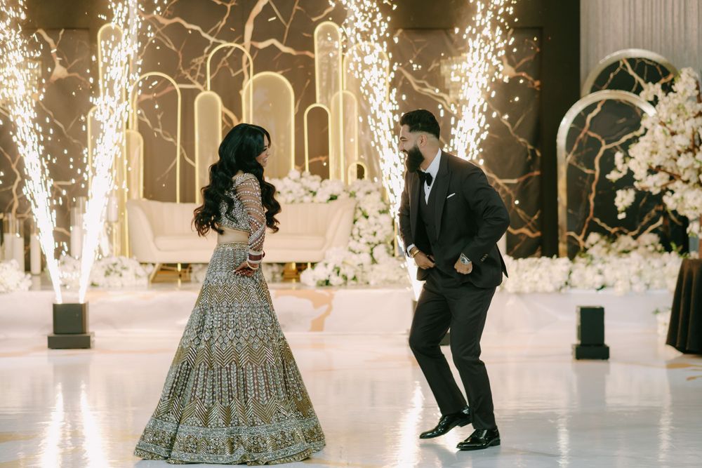 A couple dances together on a white floor with sparklers and elegant wedding decor in the background.