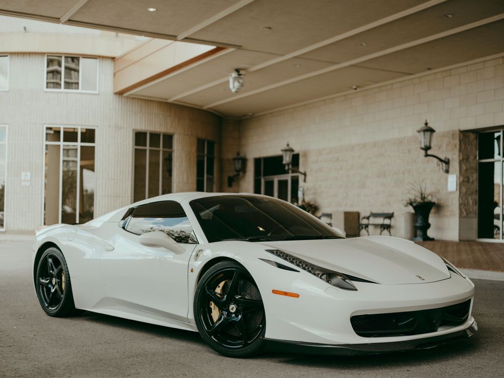 A white Ferrari 458 Italia supercar parked under a covered entrance of an elegant building.