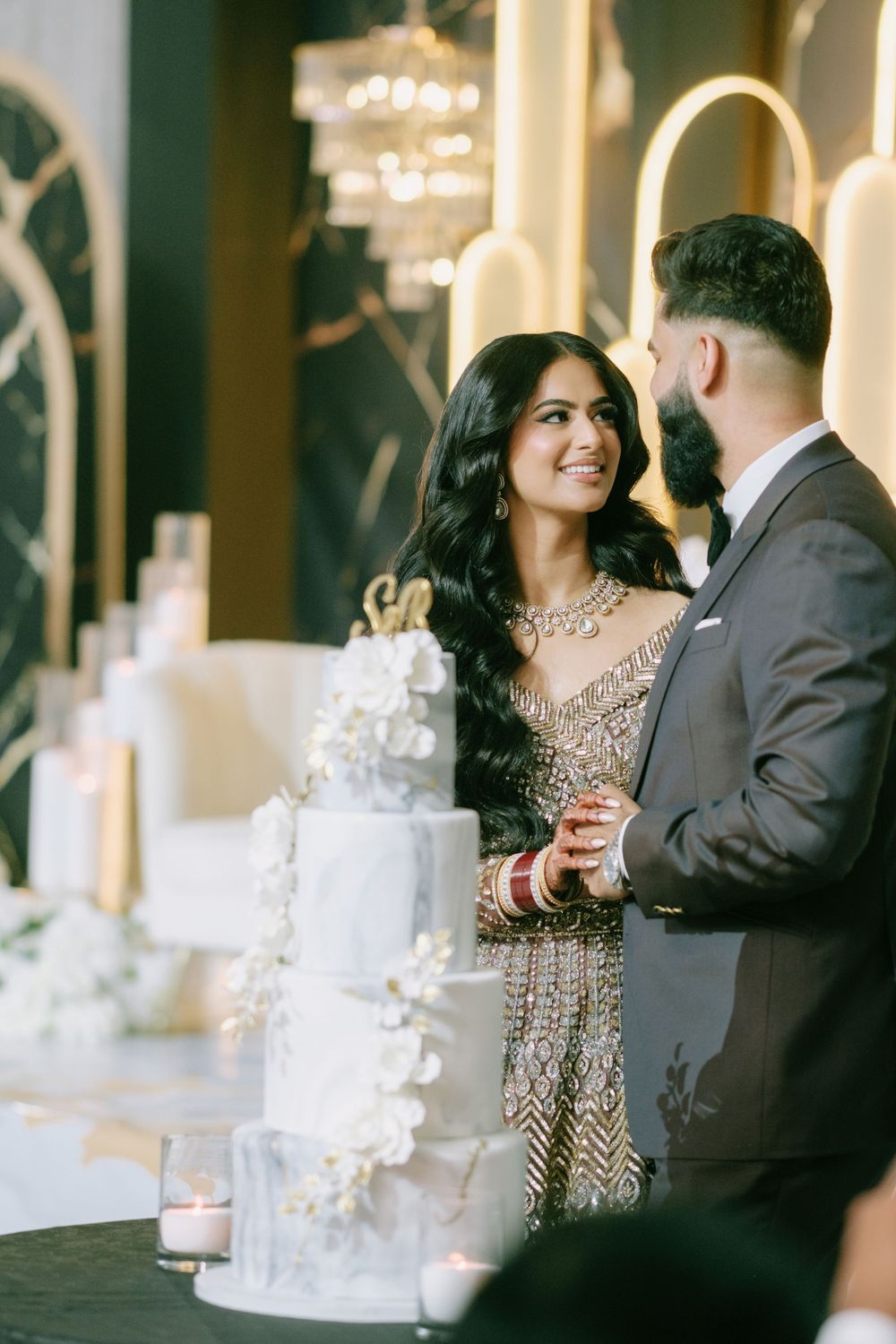Couple celebrating at an elegant wedding reception with an ornate white tiered cake and decorative candlelit table setting.
