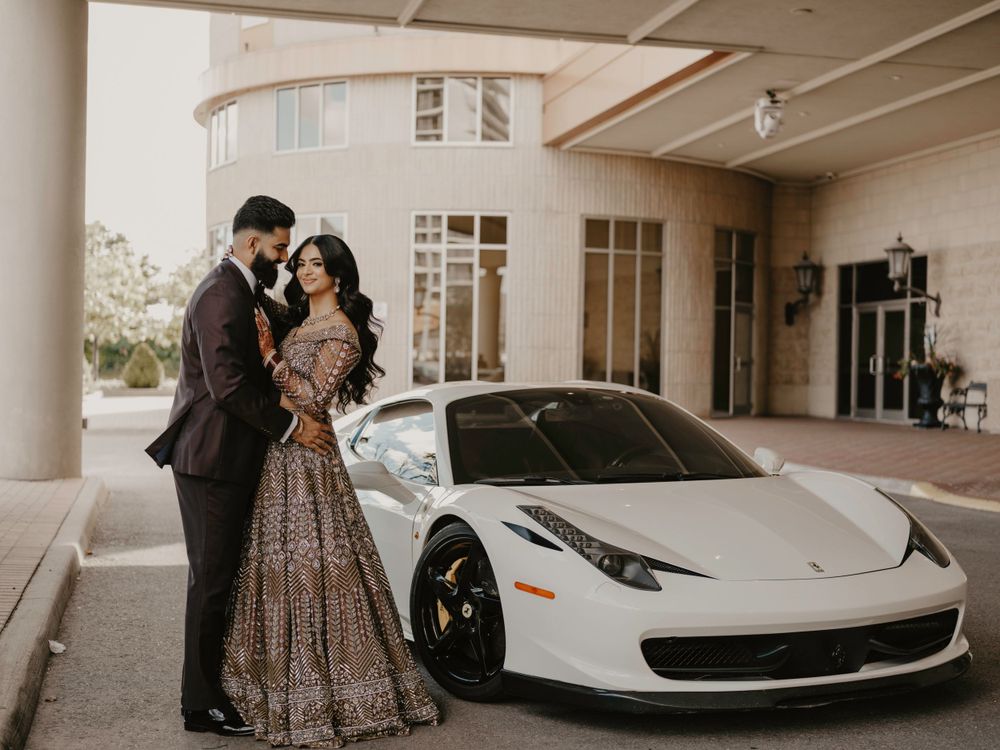 A couple poses elegantly beside a white Ferrari 458 Italia at an upscale venue entrance.