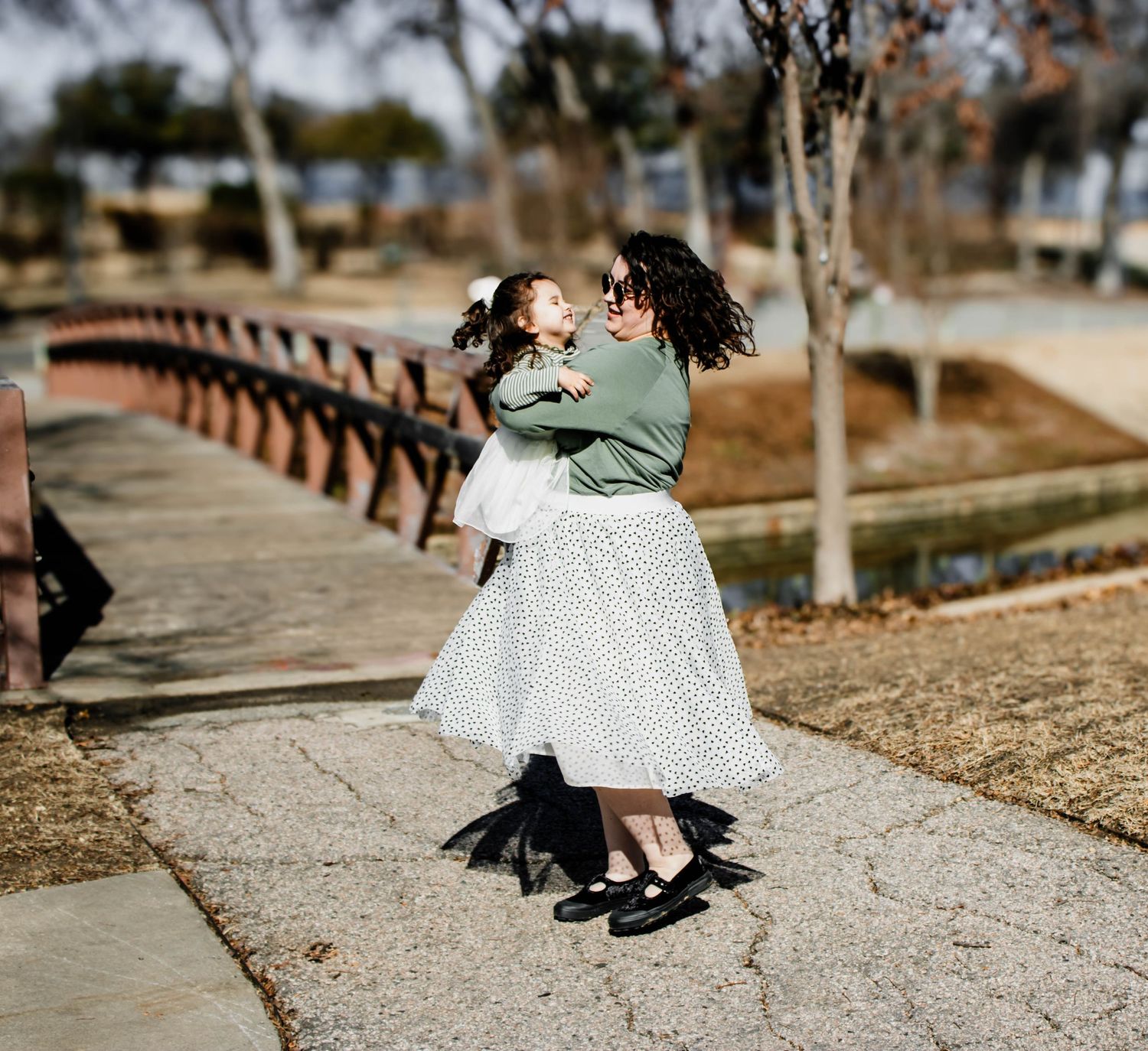 Two dancers in vintage attire share a romantic waltz on a pathway near a bridge.