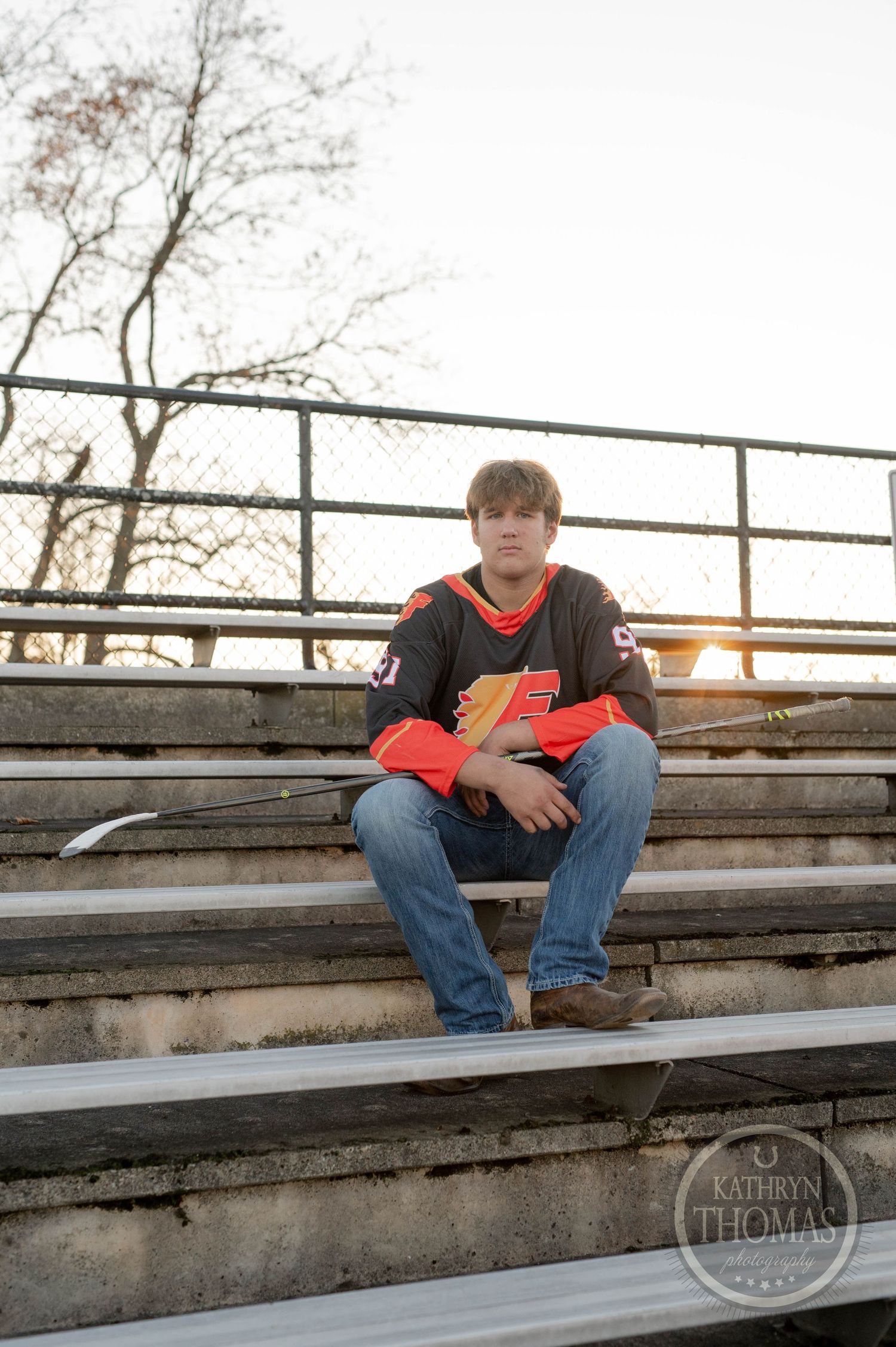 Student athlete sits on outdoor stadium bleachers wearing sports jersey and jeans.