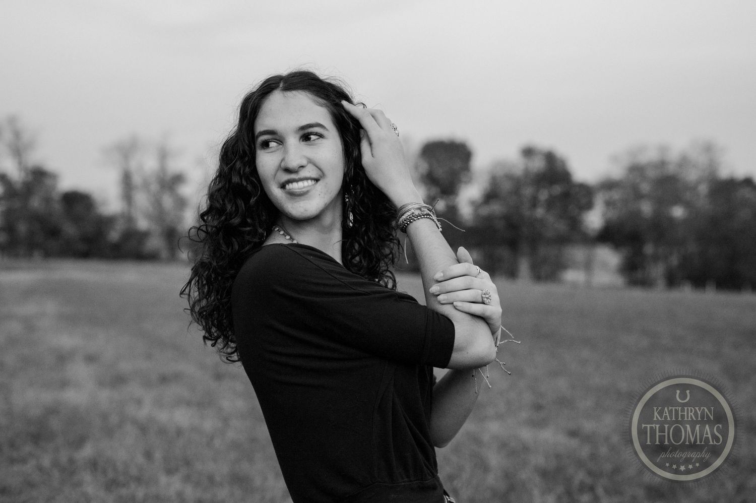 Black and white portrait of person with curly hair embracing themselves outdoors.