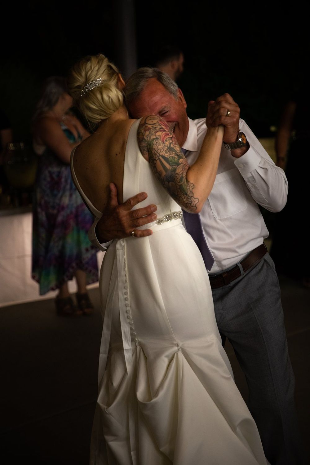 A couple shares a romantic dance at their wedding reception, with the bride wearing a fitted white dress.