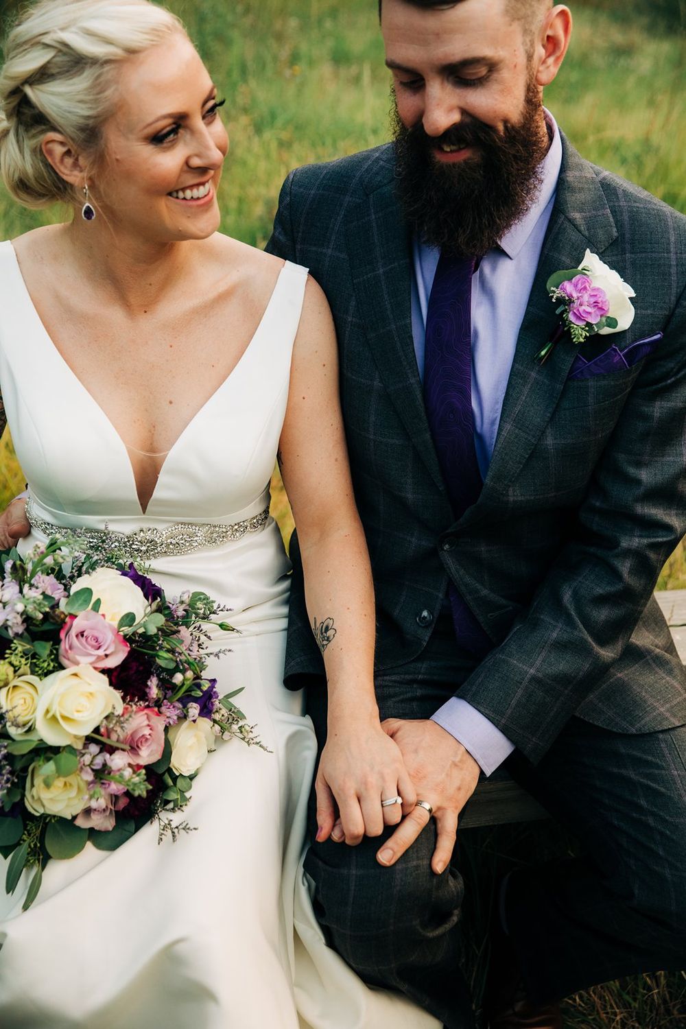 A newlywed couple shares an intimate moment outdoors with the bride holding a pink and white floral bouquet.