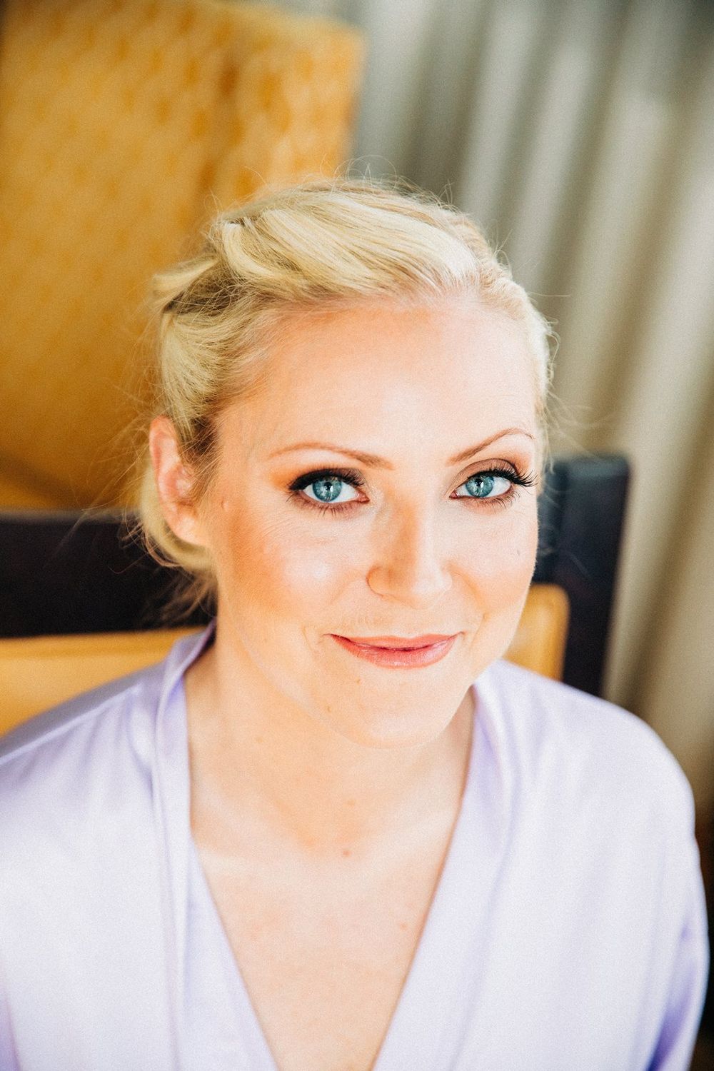 Portrait of someone with blonde hair and blue eyes wearing a light lavender top, smiling warmly at the camera.