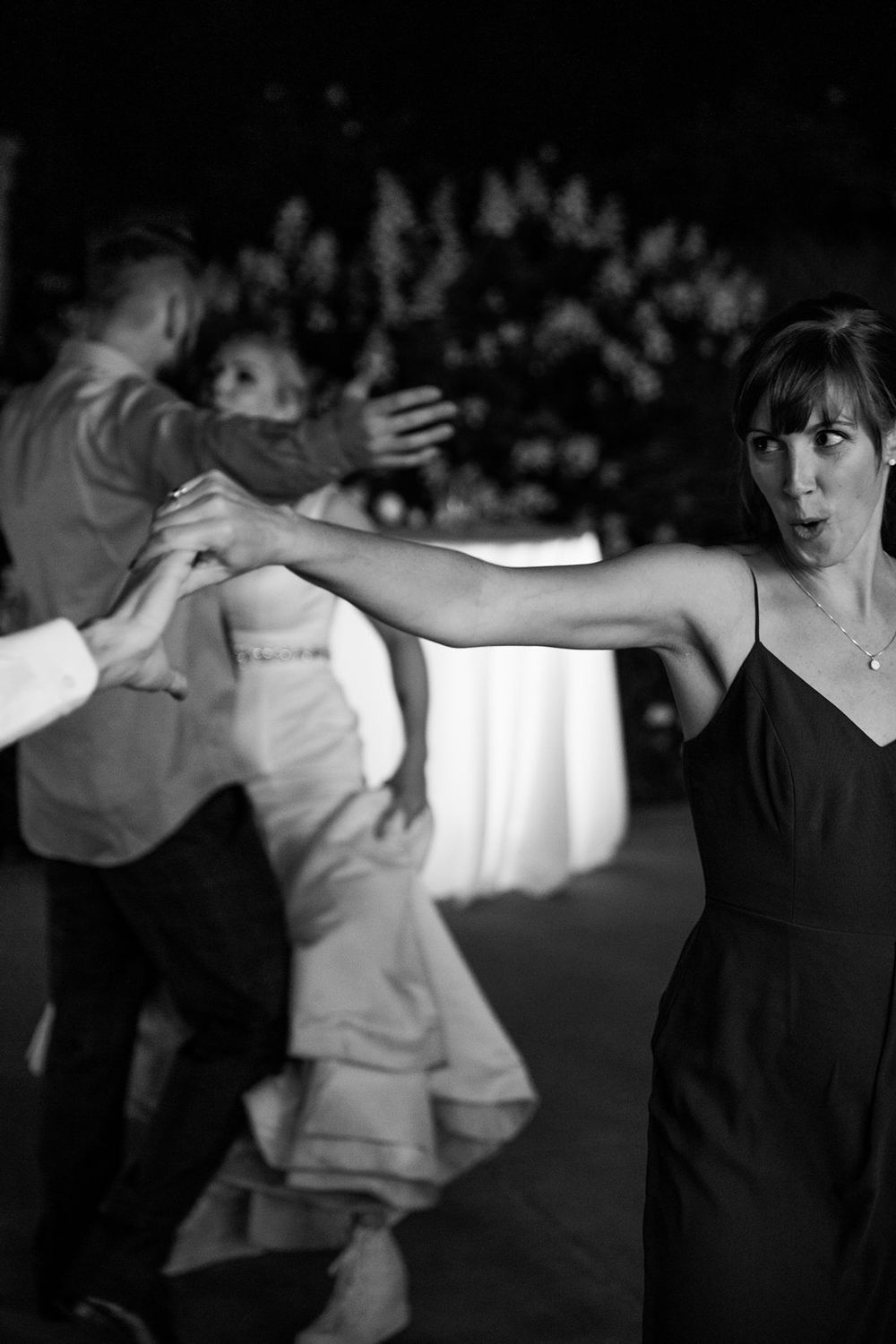 Dancers move expressively on a dark dance floor, with a woman in black dress gesturing in the foreground.