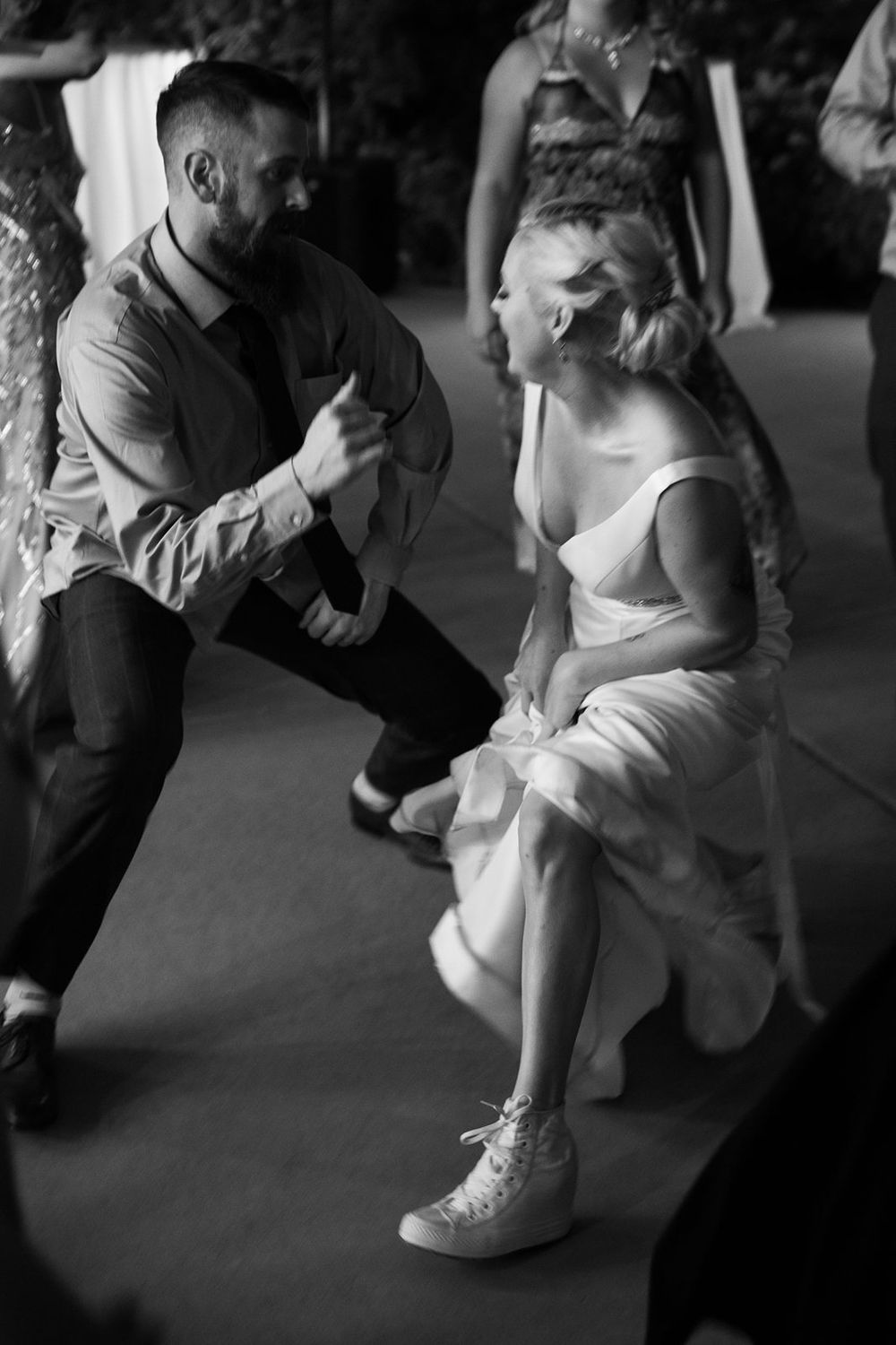 Wedding couple dances energetically at reception with bride wearing sneakers under her white dress.