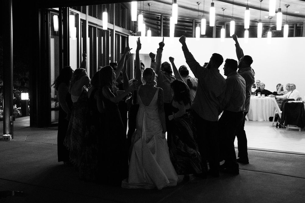 A silhouetted group of wedding guests dance and celebrate on the dance floor at a reception venue.