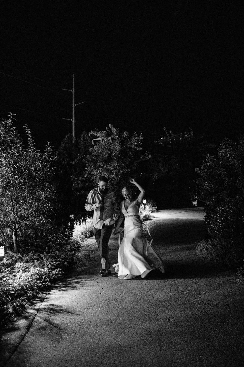 A couple dances together on an illuminated garden path at night, with the bride's white dress glowing in the darkness.