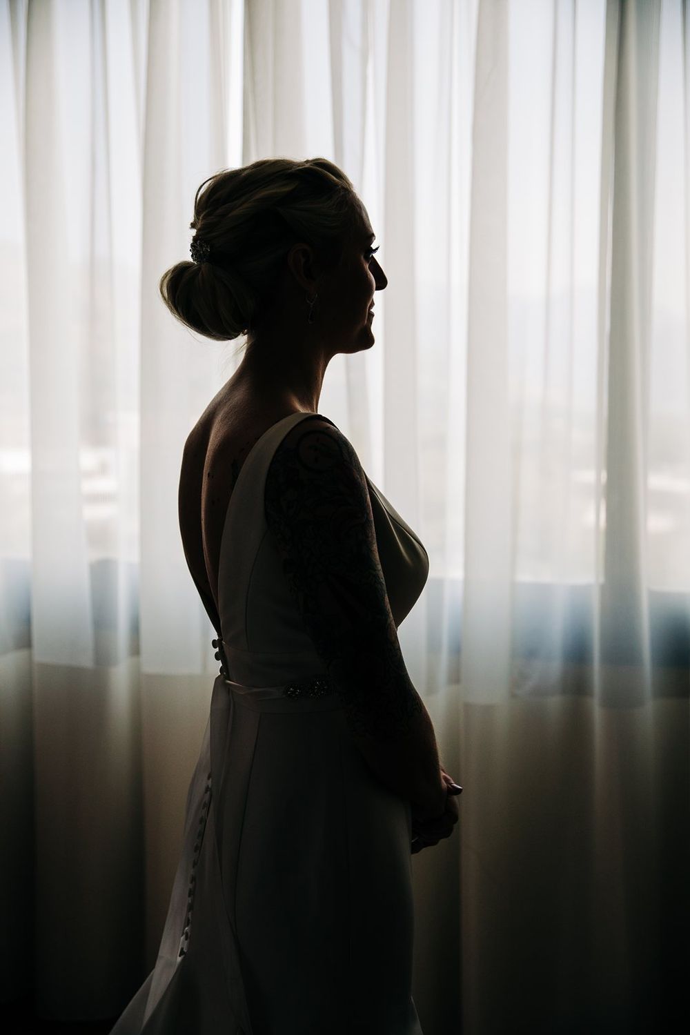 Silhouette of a woman in elegant attire against white curtains bathed in soft natural light.