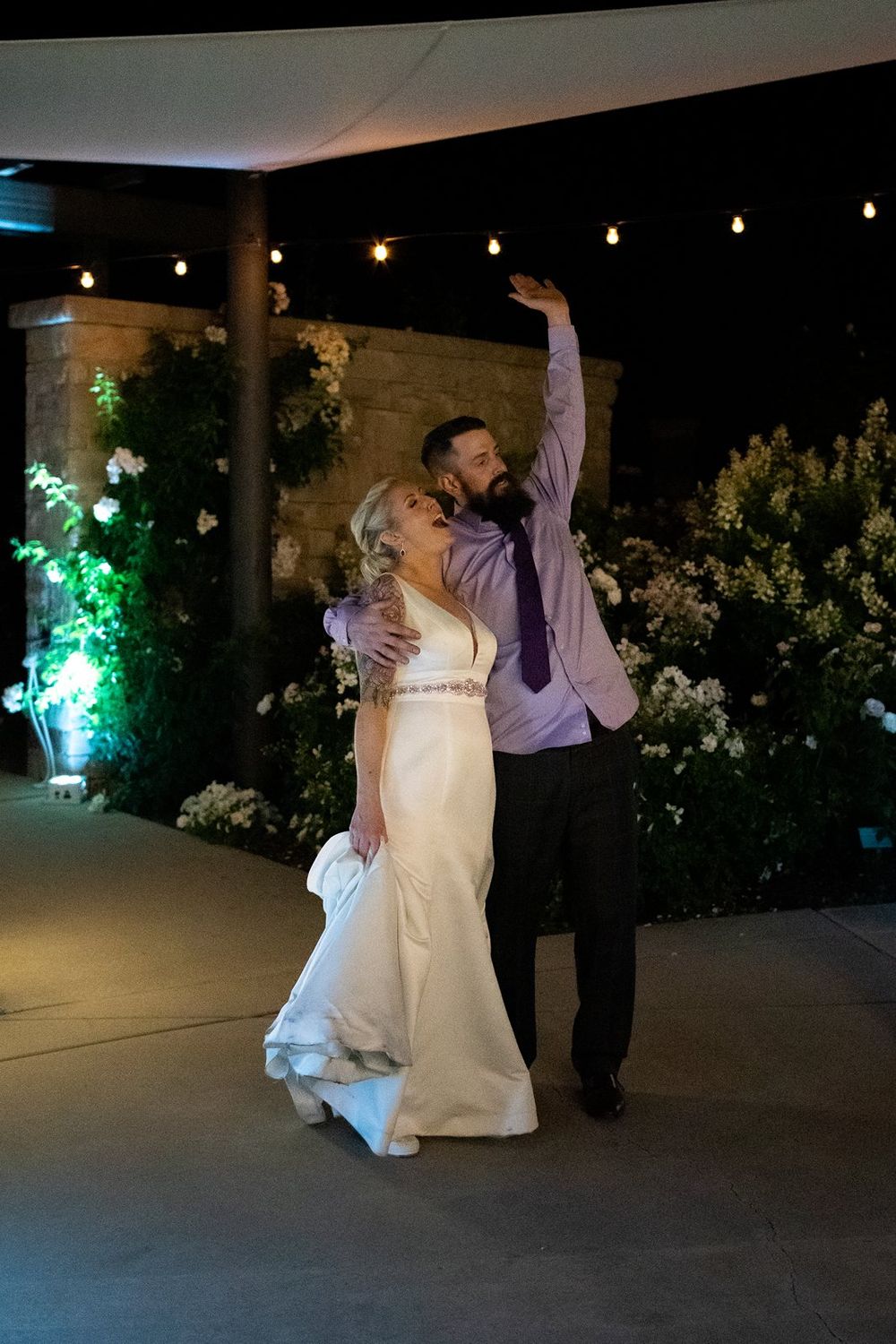 A couple dancing together at their evening wedding reception with string lights overhead.
