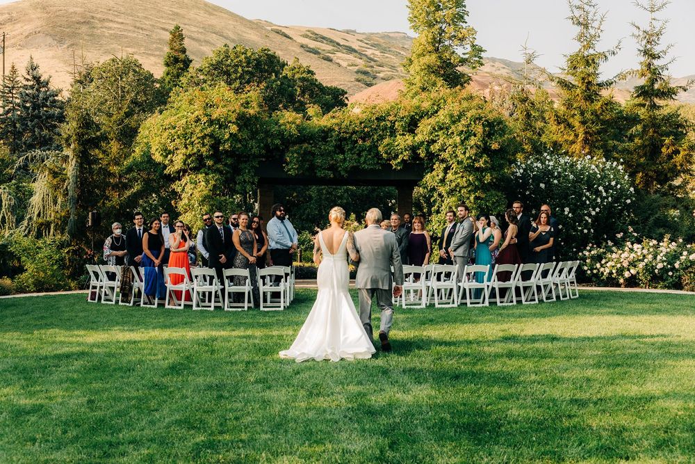 Beautiful outdoor wedding ceremony set on a lush green lawn with white chairs and mountain backdrop in summer.