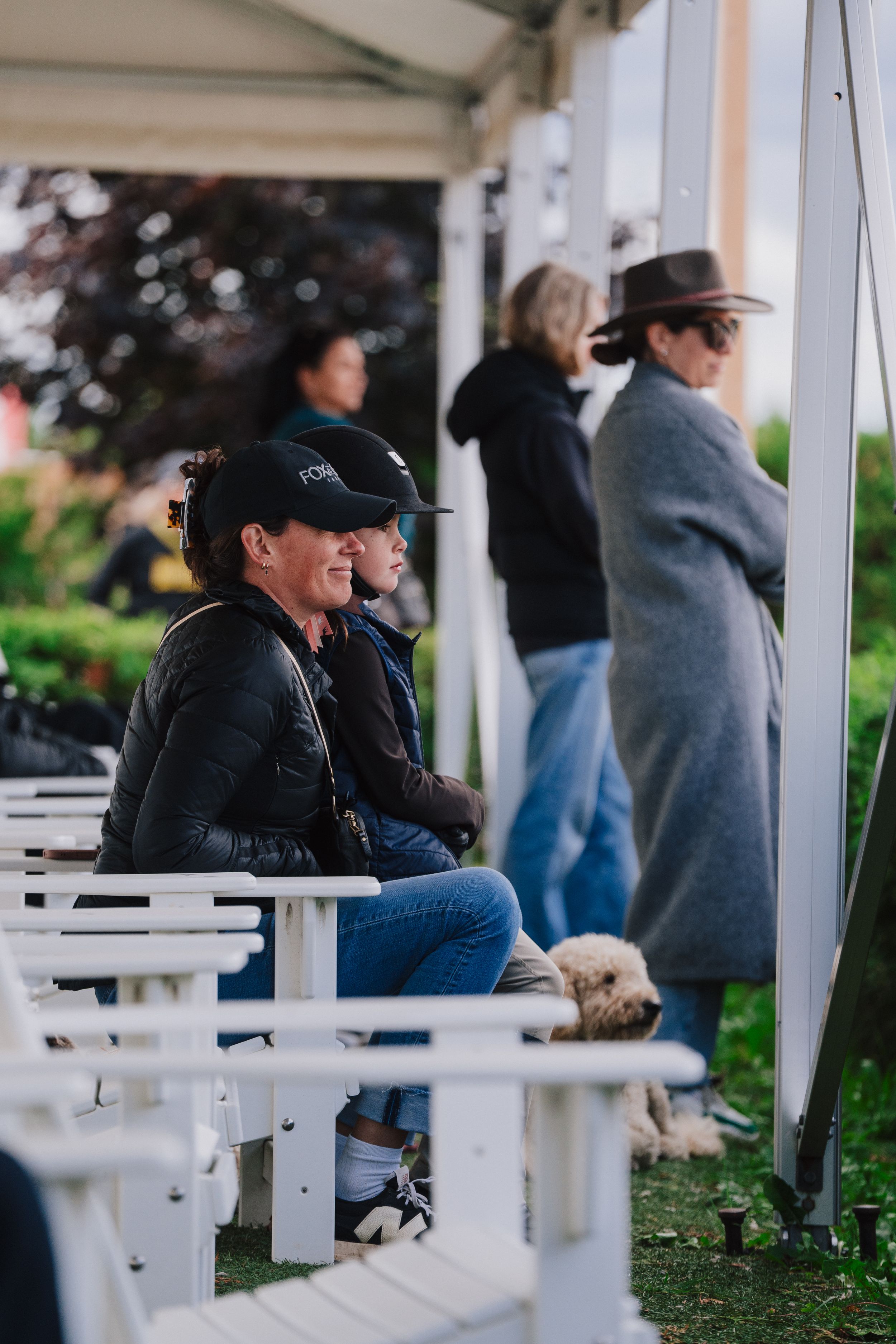 People sit and gather under a white covered porch area on a sunny day.
