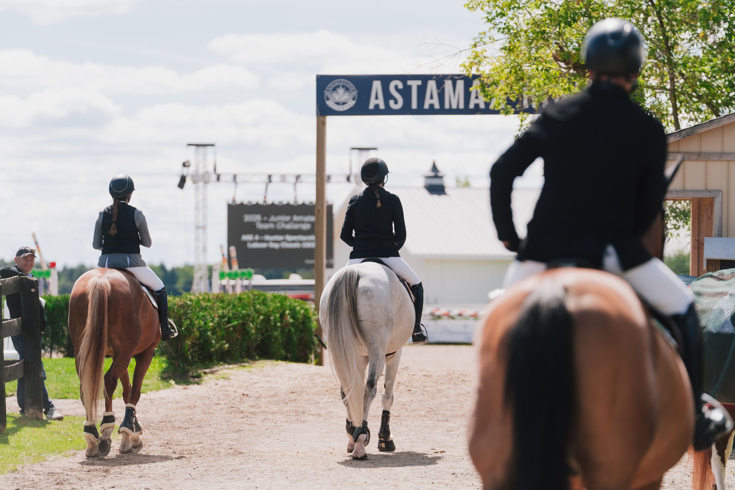 Riders in helmets and dark jackets walking along a waterfront path near an Astana sign.
