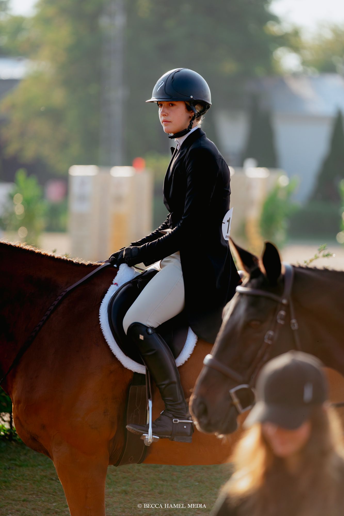 An equestrian rider in formal black show attire sits atop a bay horse during a competition event.