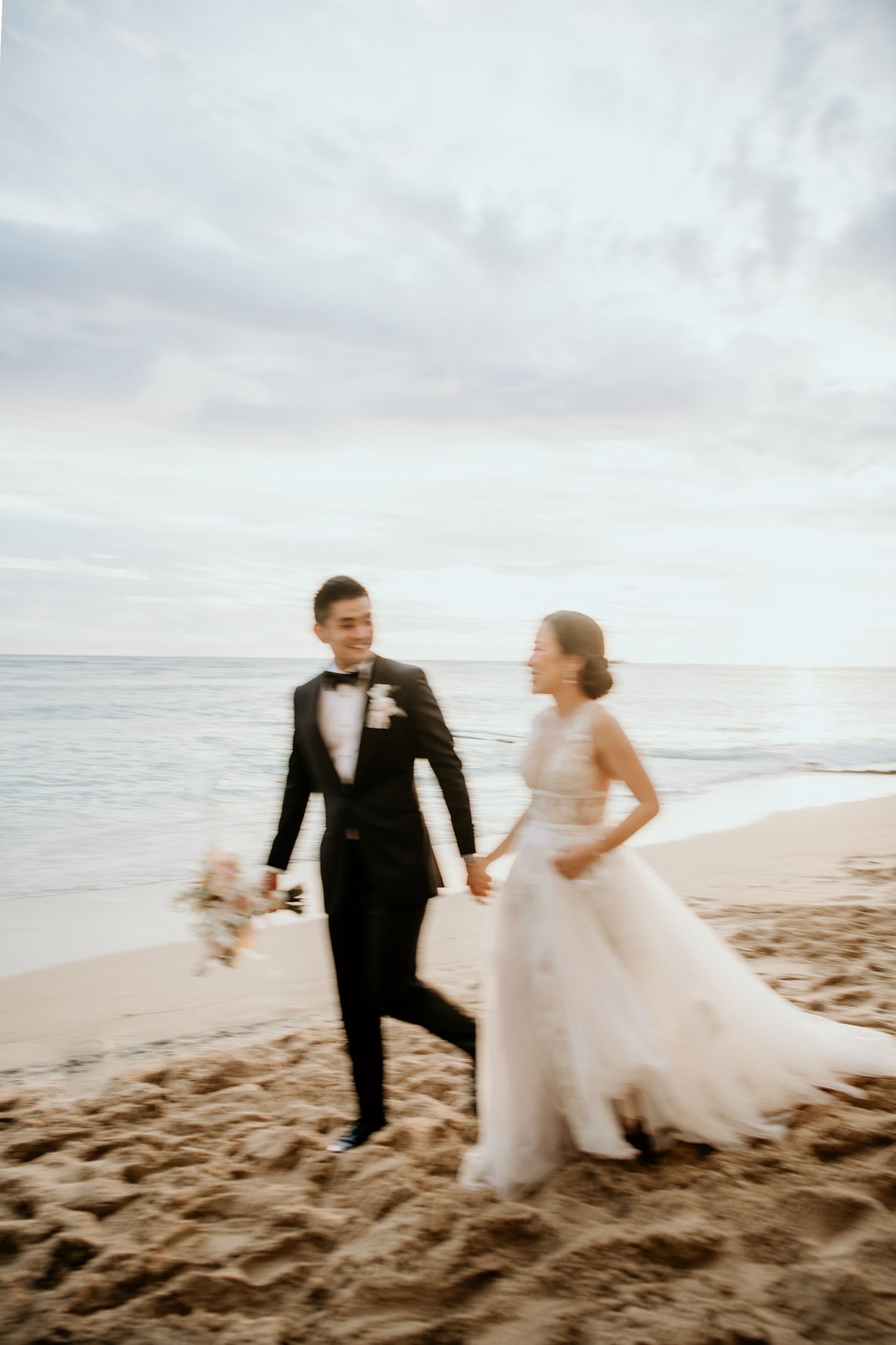 A couple in wedding attire walk together holding hands photographed blurred at a slow shutter speed at sunset.