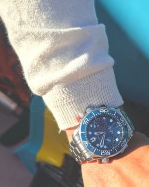 A silver dive watch with blue bezel worn over a white sweater sleeve.