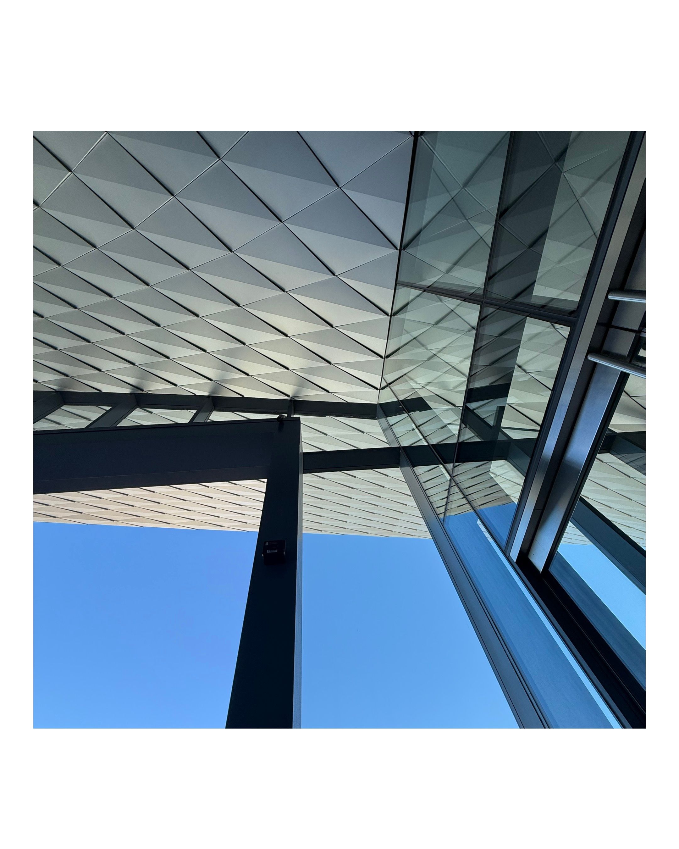 Modern architectural ceiling with geometric diamond patterns against blue sky.