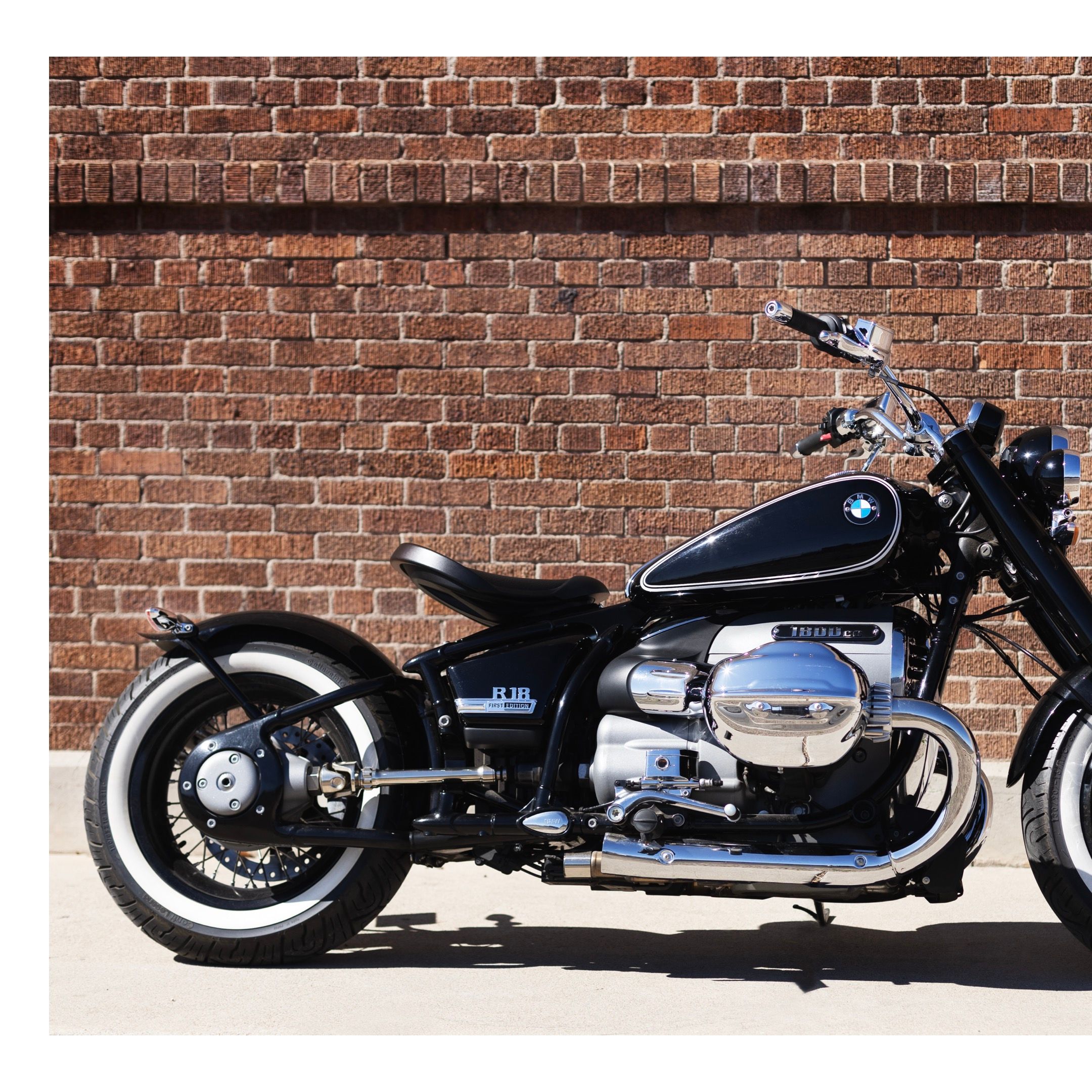 A classic BMW motorcycle with whitewall tires parked against a brick wall.