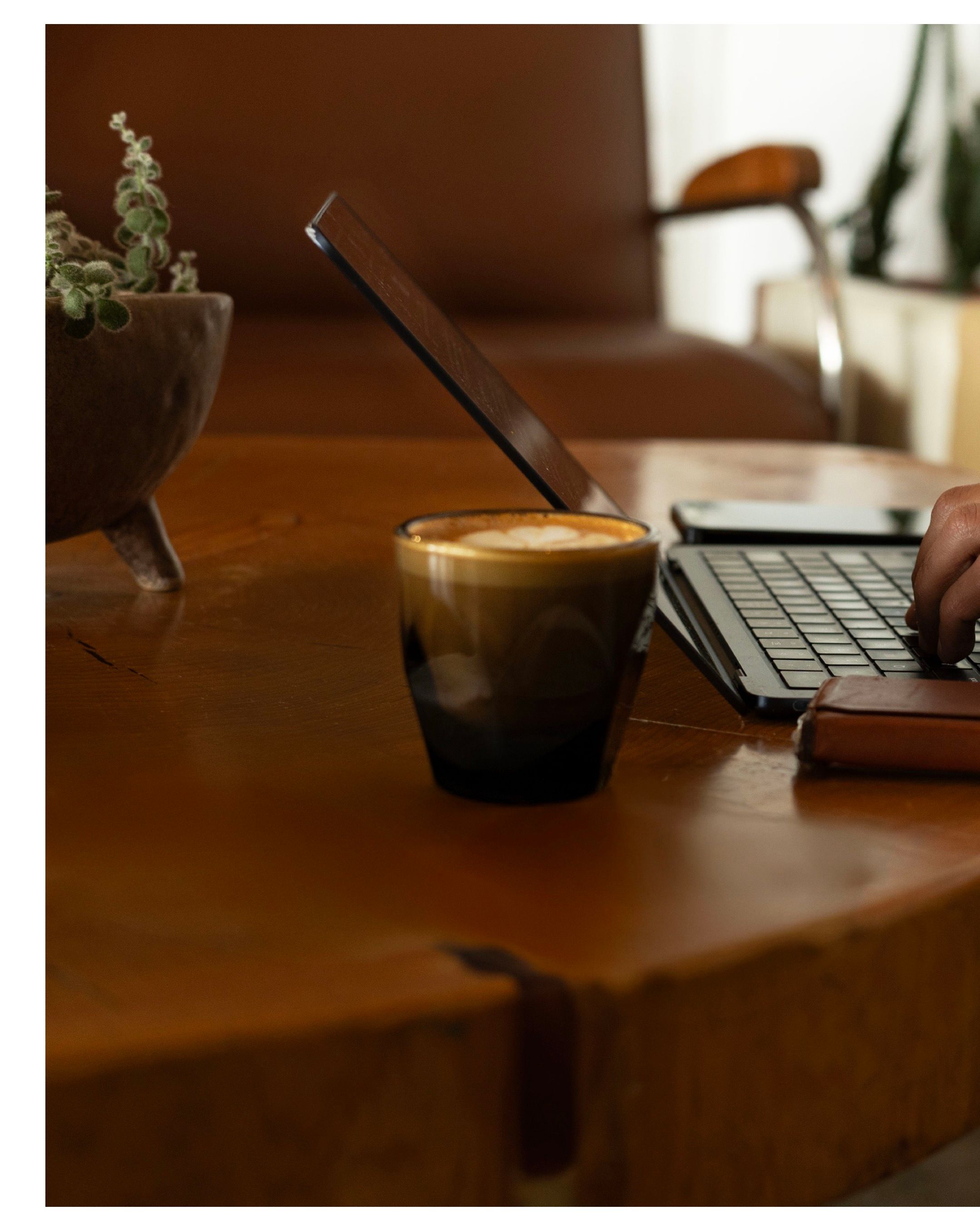 A cortado drink and laptop on a wooden desk with a small potted plant.