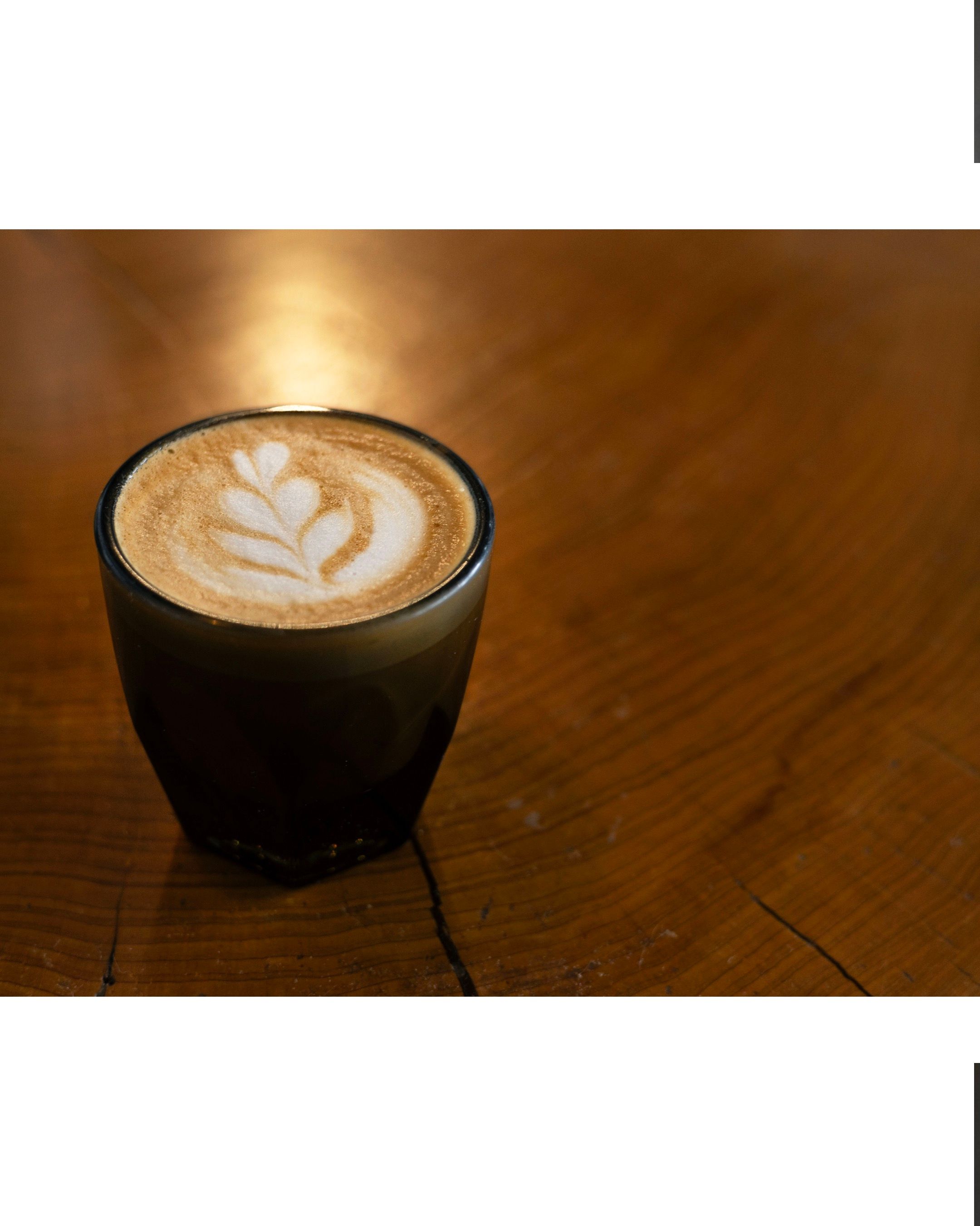 Cortado art featuring a leaf design in an amber glass cup on wooden table.