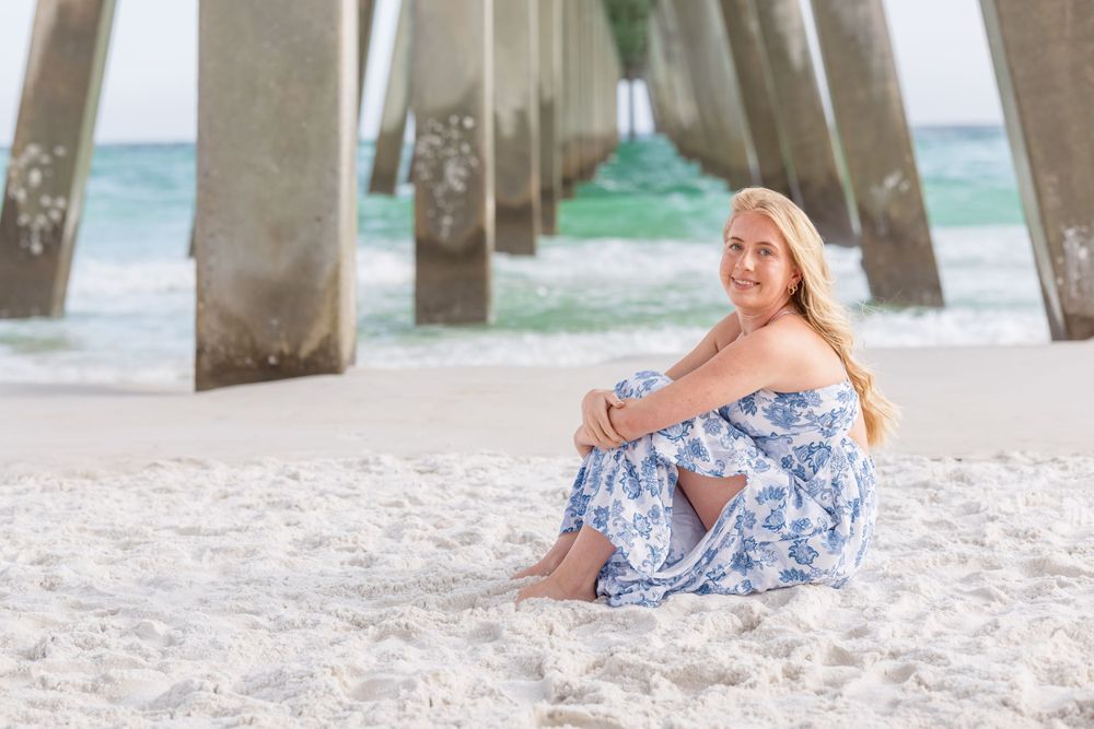 A dreamy beach portrait under a pier with soft blue and white tones on a sandy shoreline.