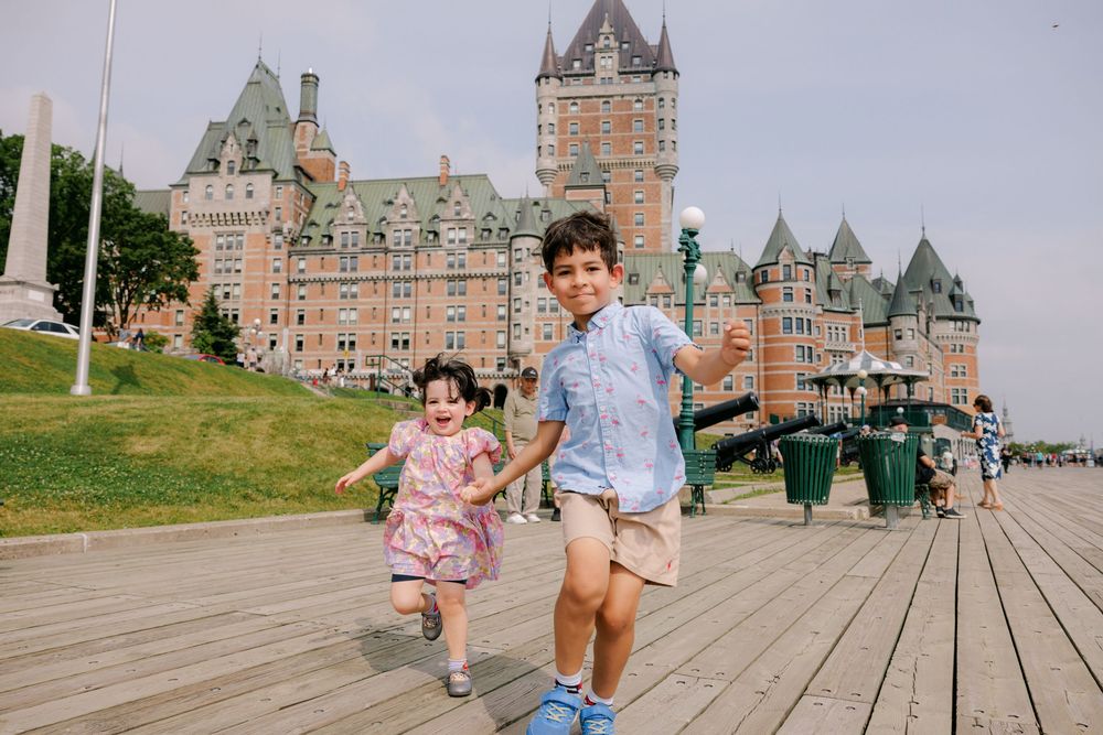 Two children running and laughing on a boardwalk in front of Château Frontenac in Quebec City, Canada.