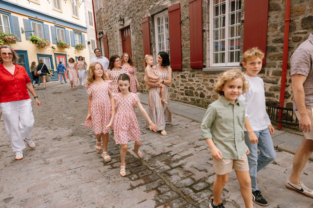 Group of children in matching pink dresses walking cobblestone streets of Old Quebec City with adults.
