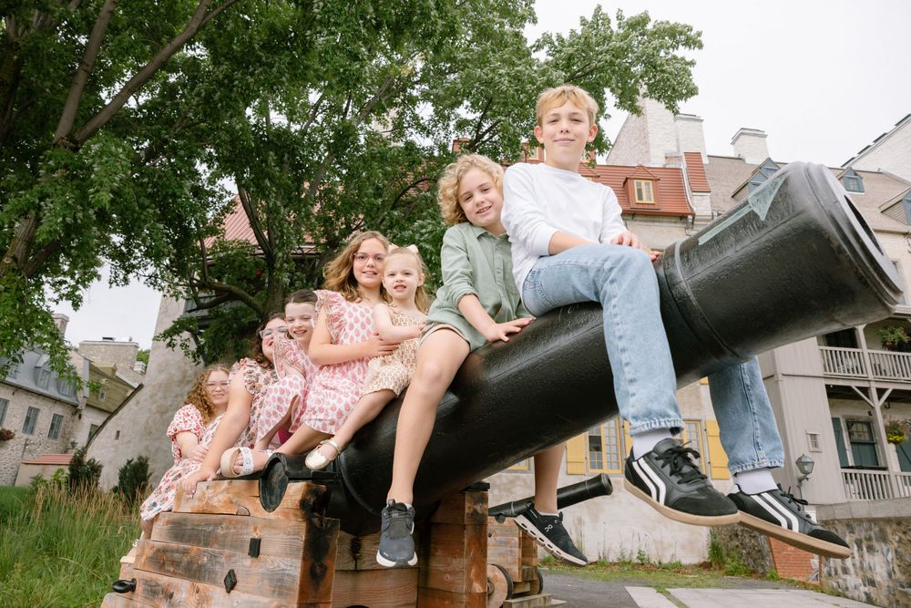 Family with children sitting on a historic cannon outdoors, smiling and posing together near old buildings.
