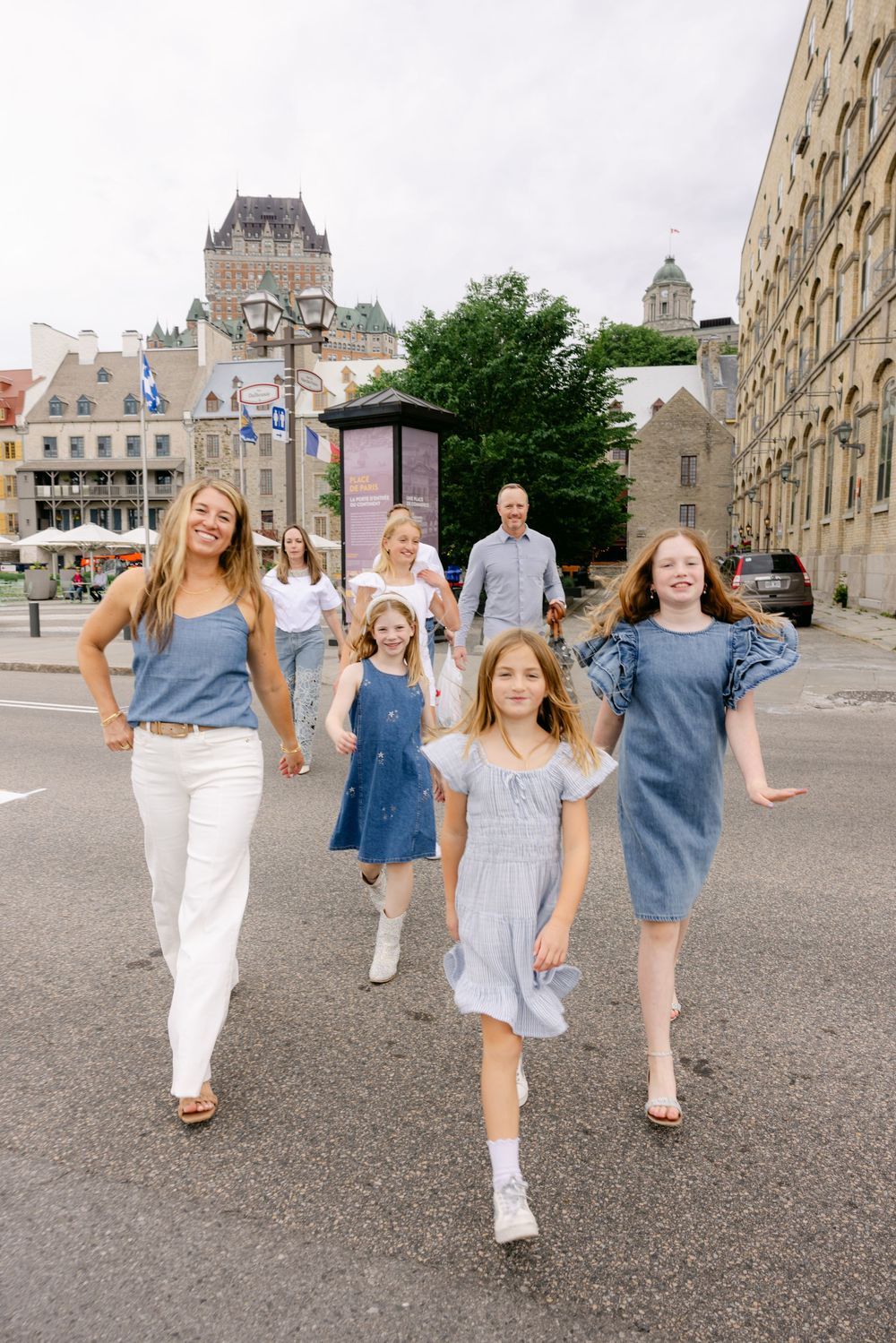 Family walking together on a street in Old Quebec City with Chateau Frontenac in the background on a cloudy day.