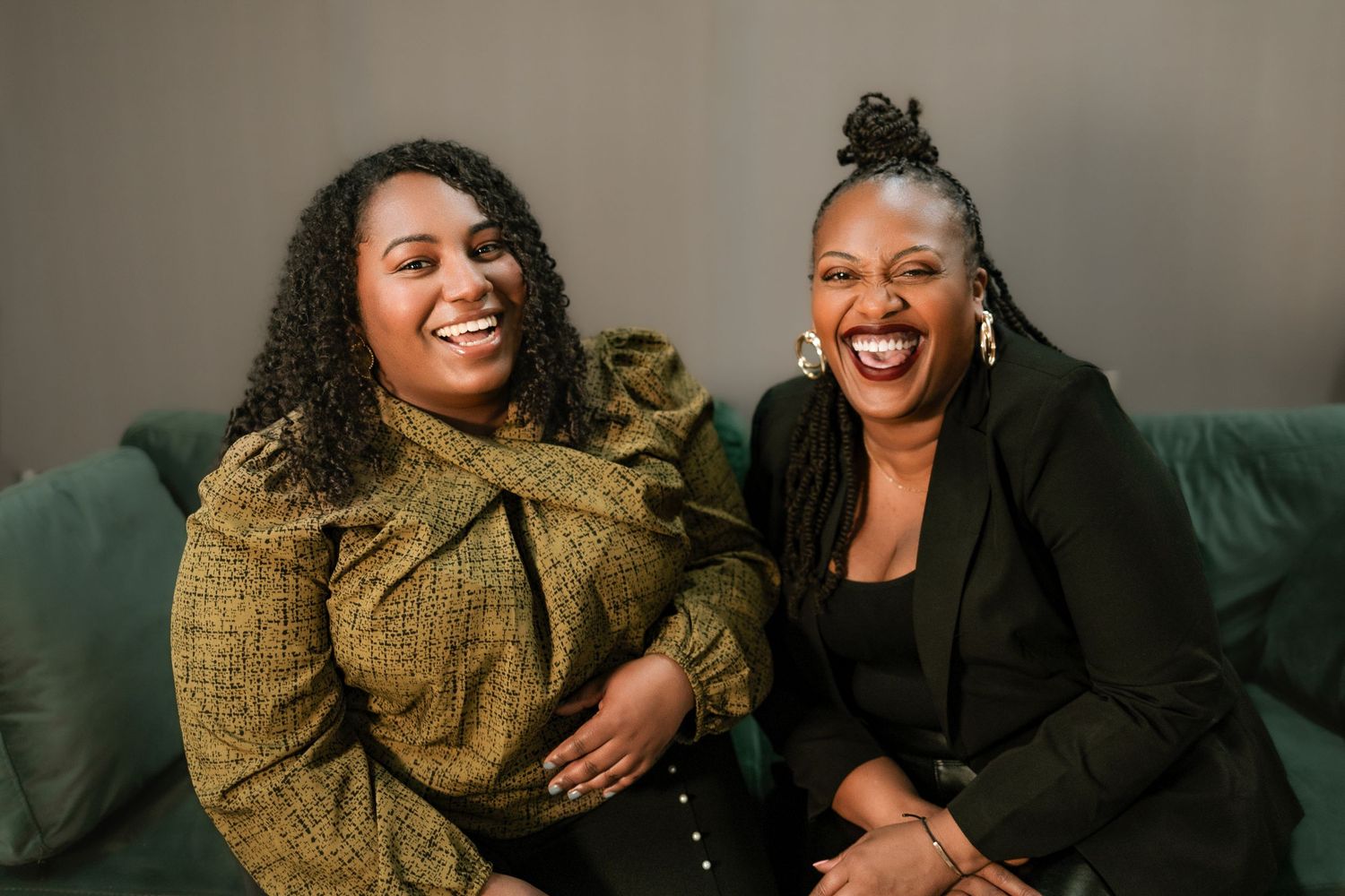 Two people laughing together while sitting on a couch in a warm, intimate setting.