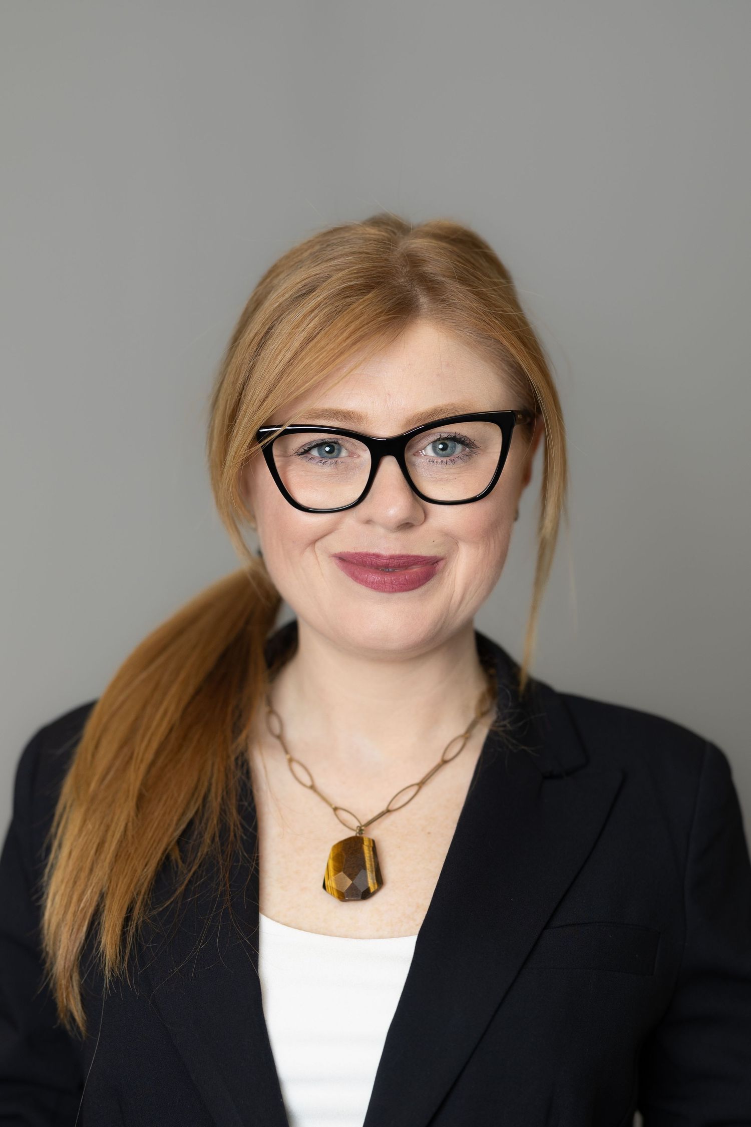 Professional headshot series showing a person in business attire with glasses and amber pendant against a gray background.