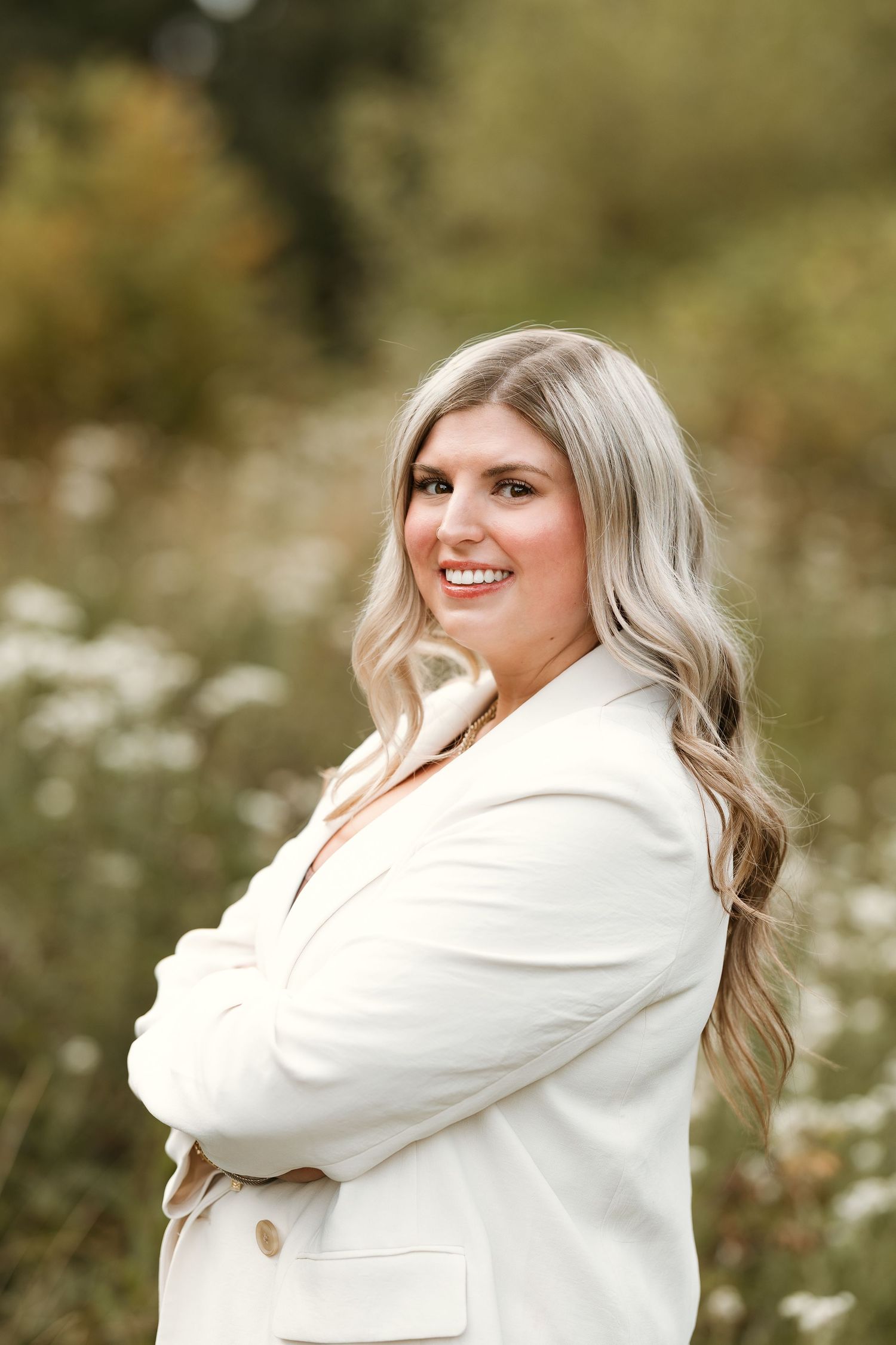 A person in a cozy white sweater poses outdoors in a field of wildflowers on a sunny autumn day.