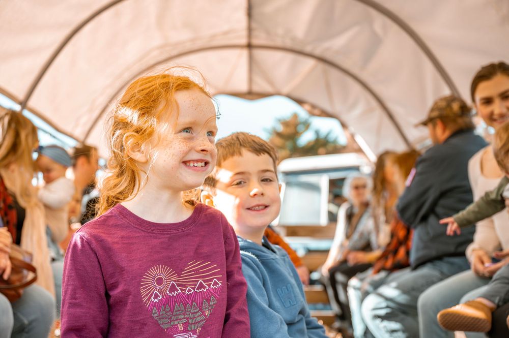 Children enjoying a ride together, laughing and smiling while sitting in what appears to be a covered wagon or carriage.