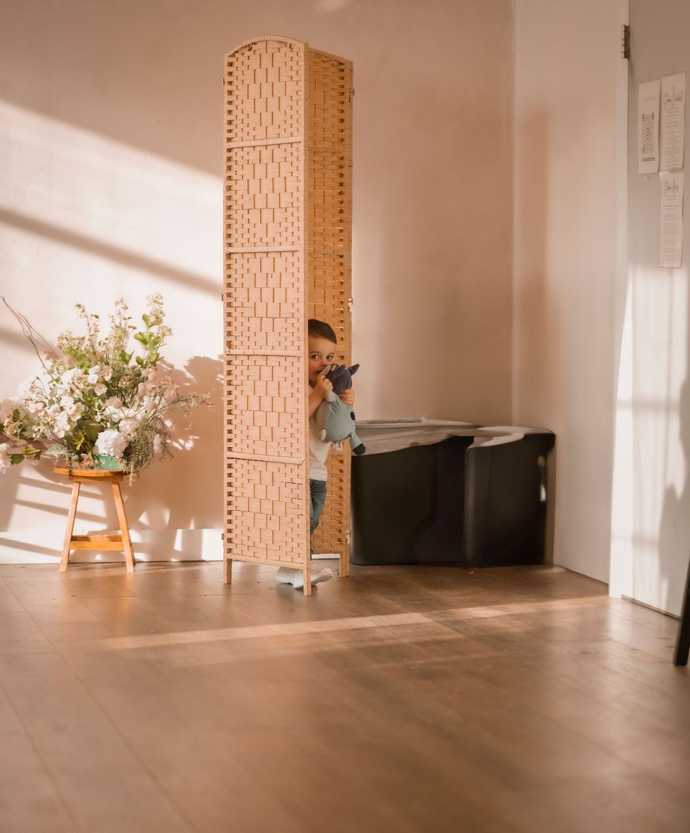 Woven room divider screen in natural tones with floral arrangement and shadows cast on hardwood floor in minimalist space.