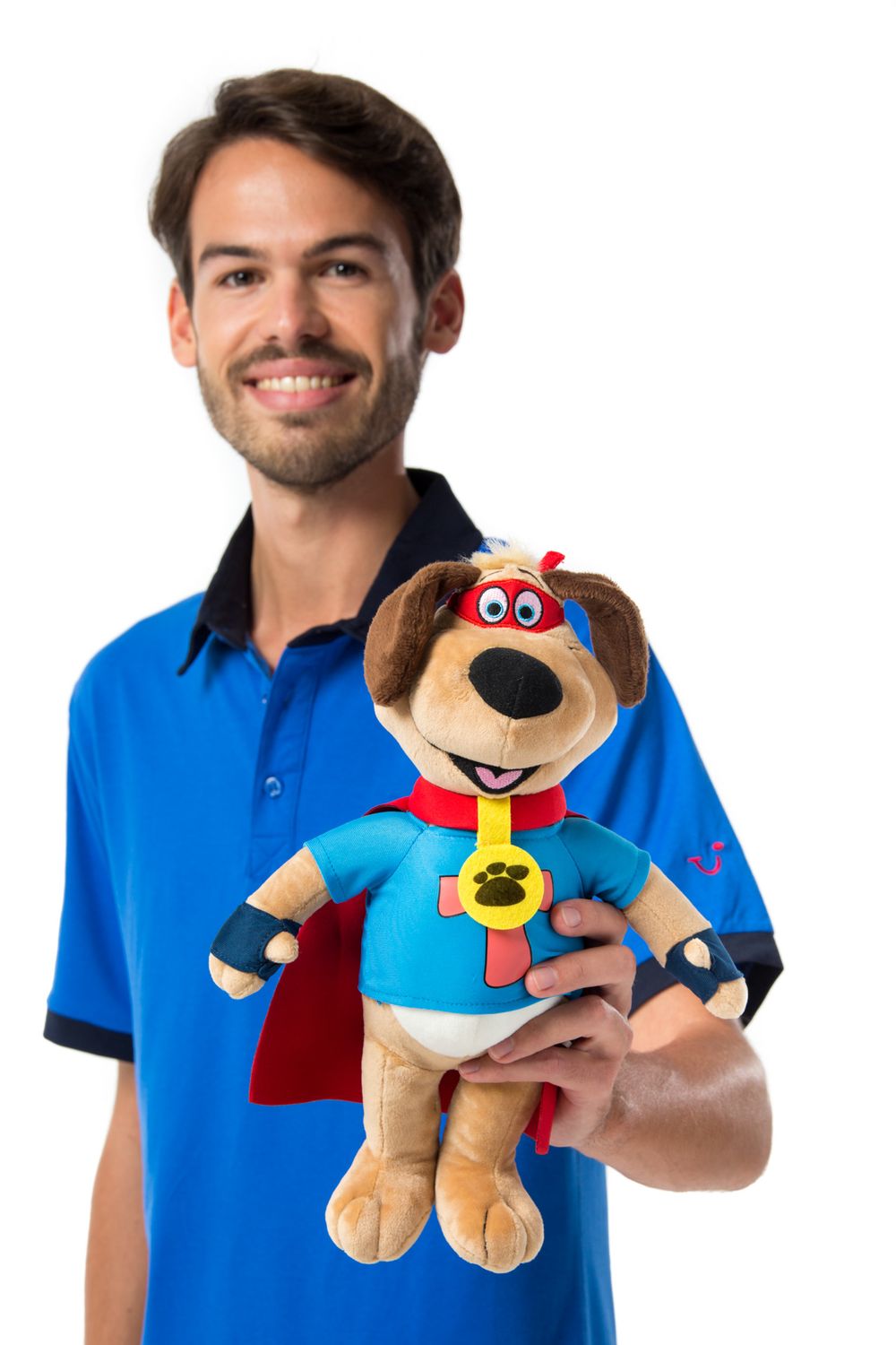 Person in blue polo shirt holding a plush stuffed dog toy wearing a superhero cape and blue shirt with medal.