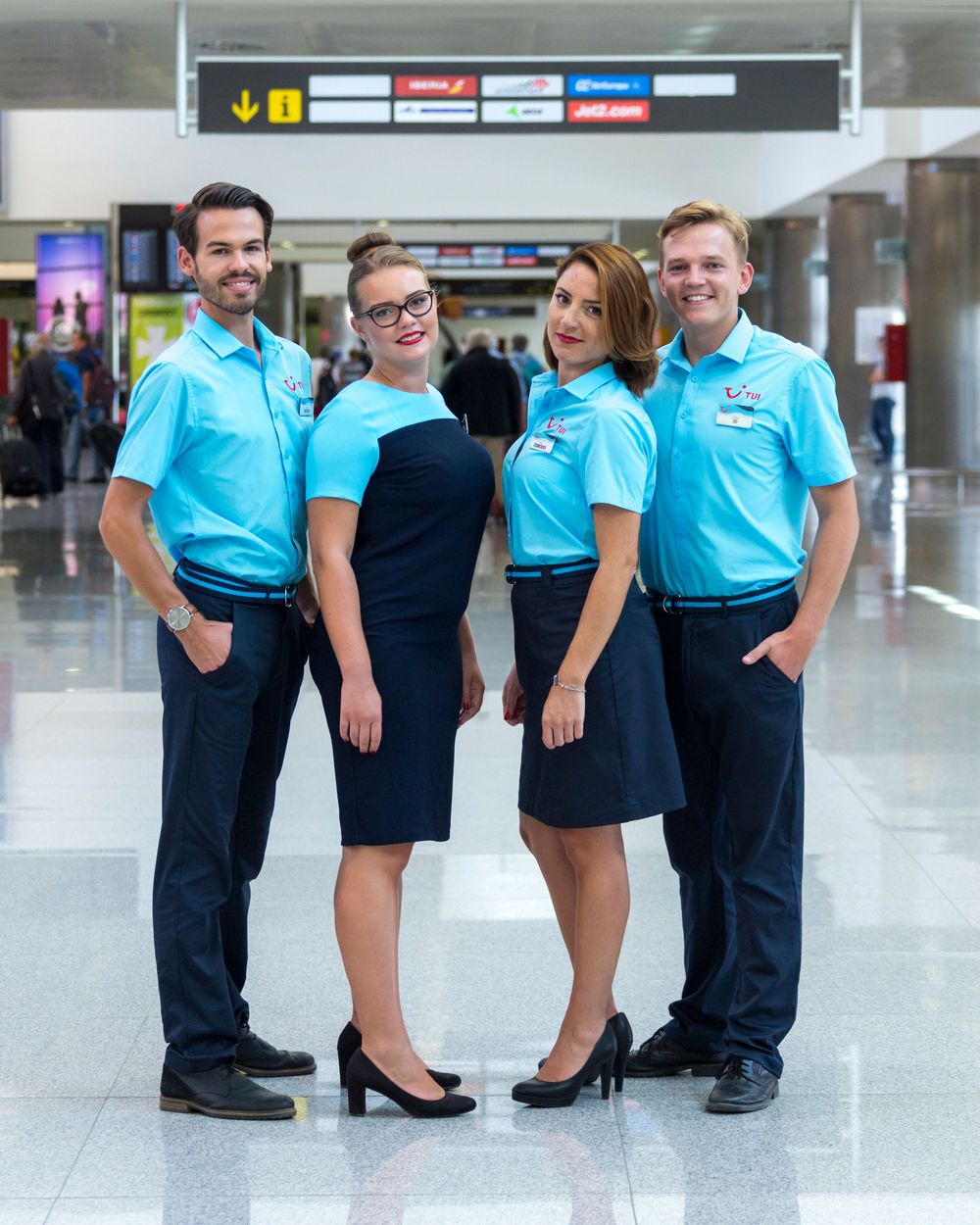 Airport staff in matching light blue uniforms and dark bottoms stand together in modern terminal concourse.