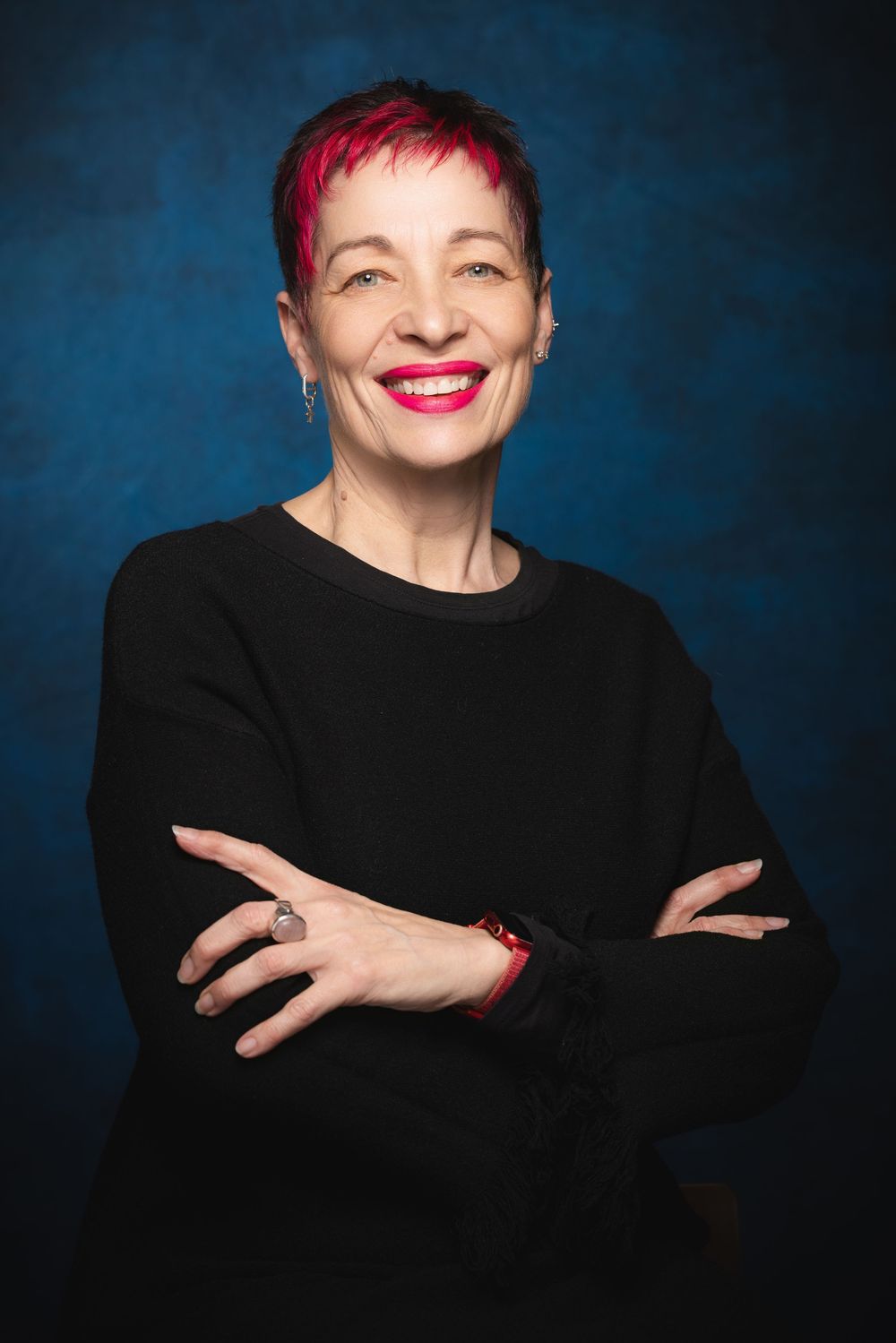 Studio headshots against a dark blue background showing a lady in a black sweater with red lipstick and short hair.