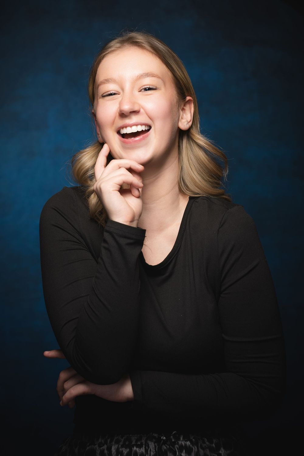 Professional headshots of a blonde female against a dark blue background, showing joyful laughter.
