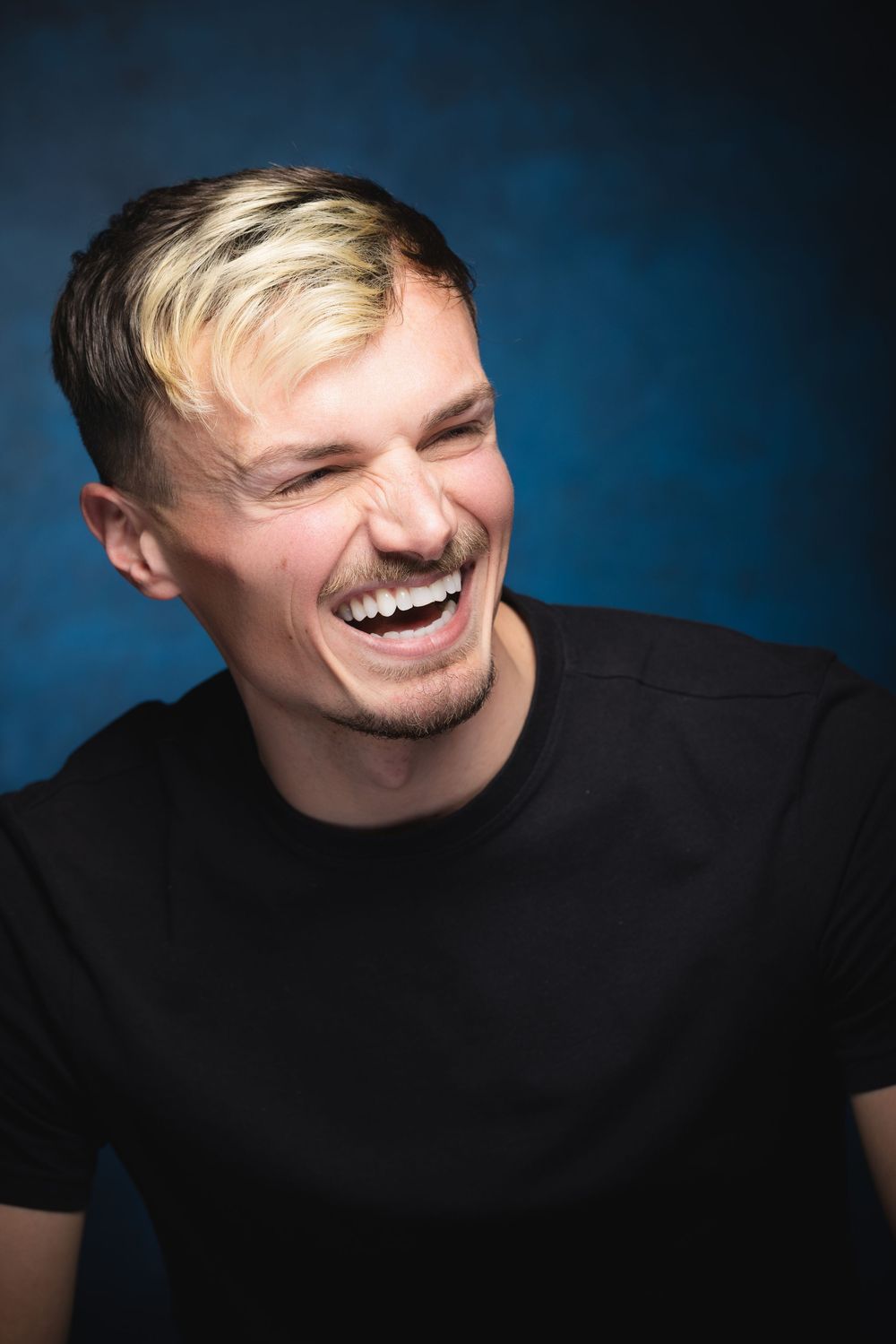 Professional headshot photography of a male laughing against a dark blue background.