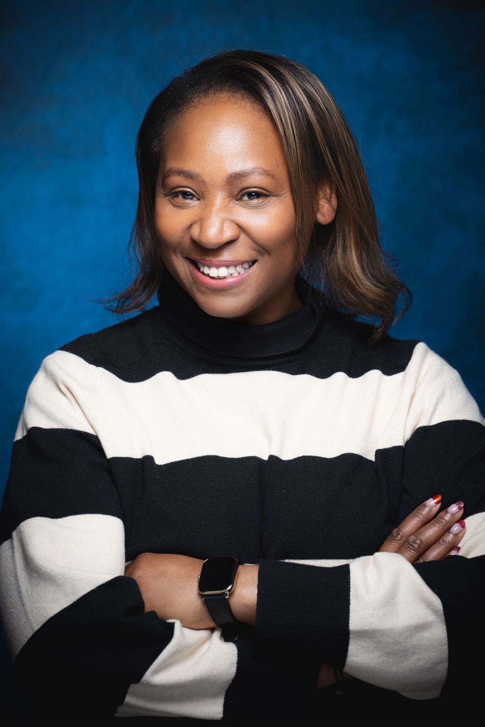 Professional portrait against blue backdrop showing a warm smile and wearing a black and white striped sweater.