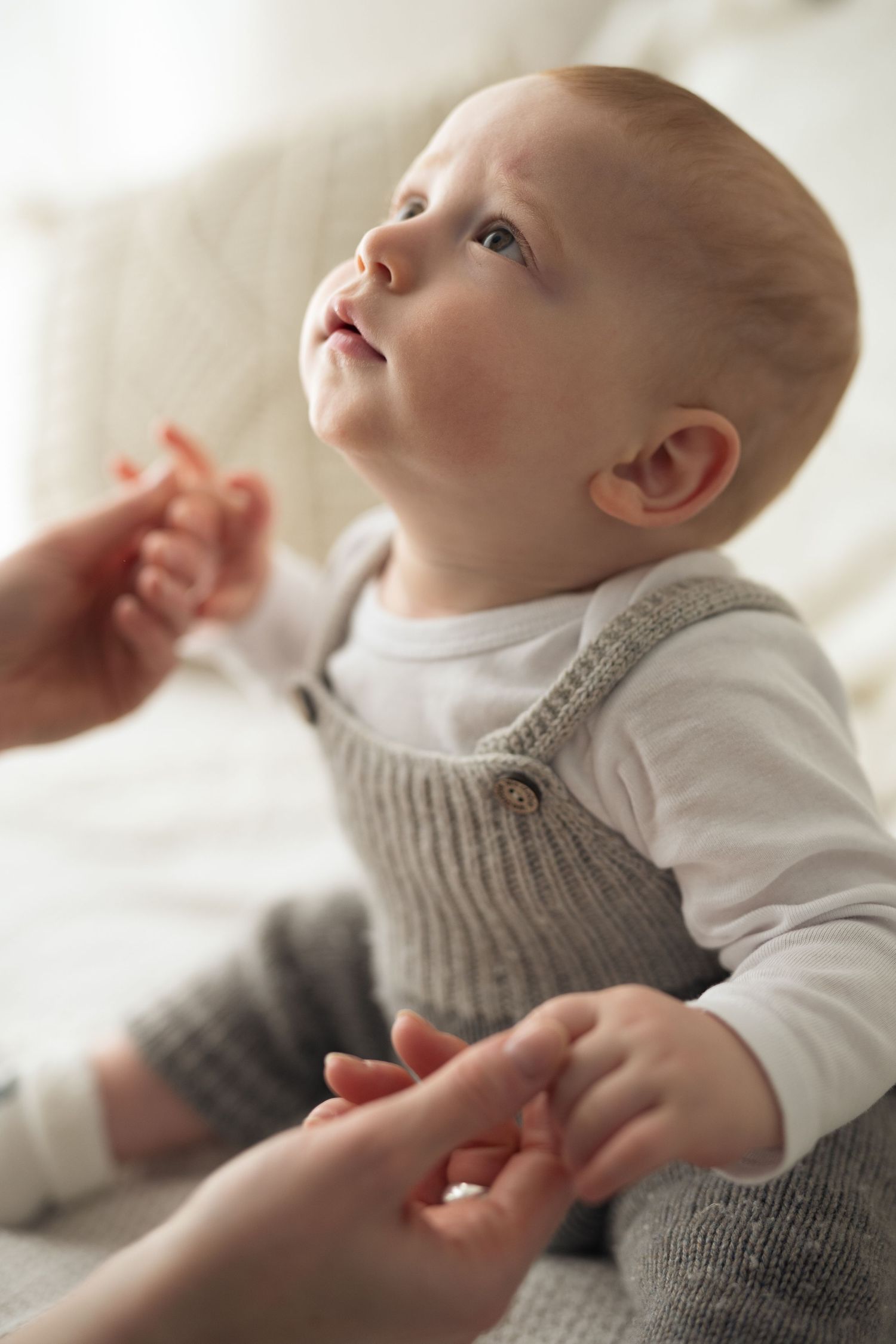 Bambino di sei mesi, guarda la mamma fuori inquadratura che gli tiene le mani