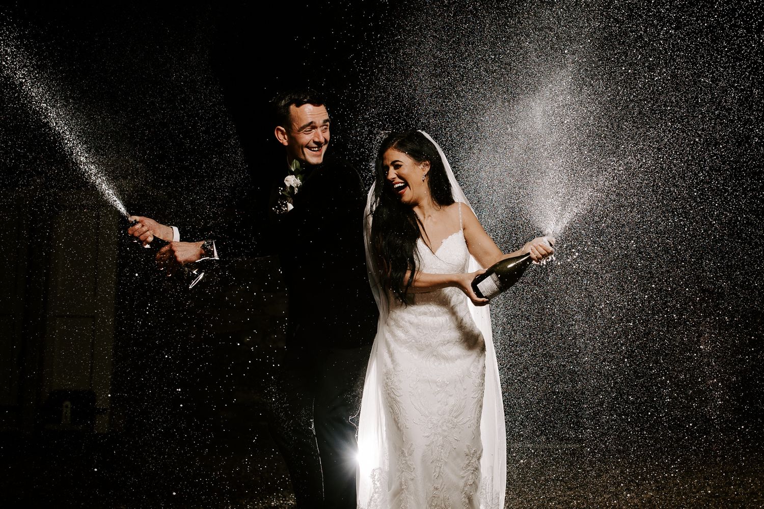 Newlyweds spraying champagne during nighttime celebration.
