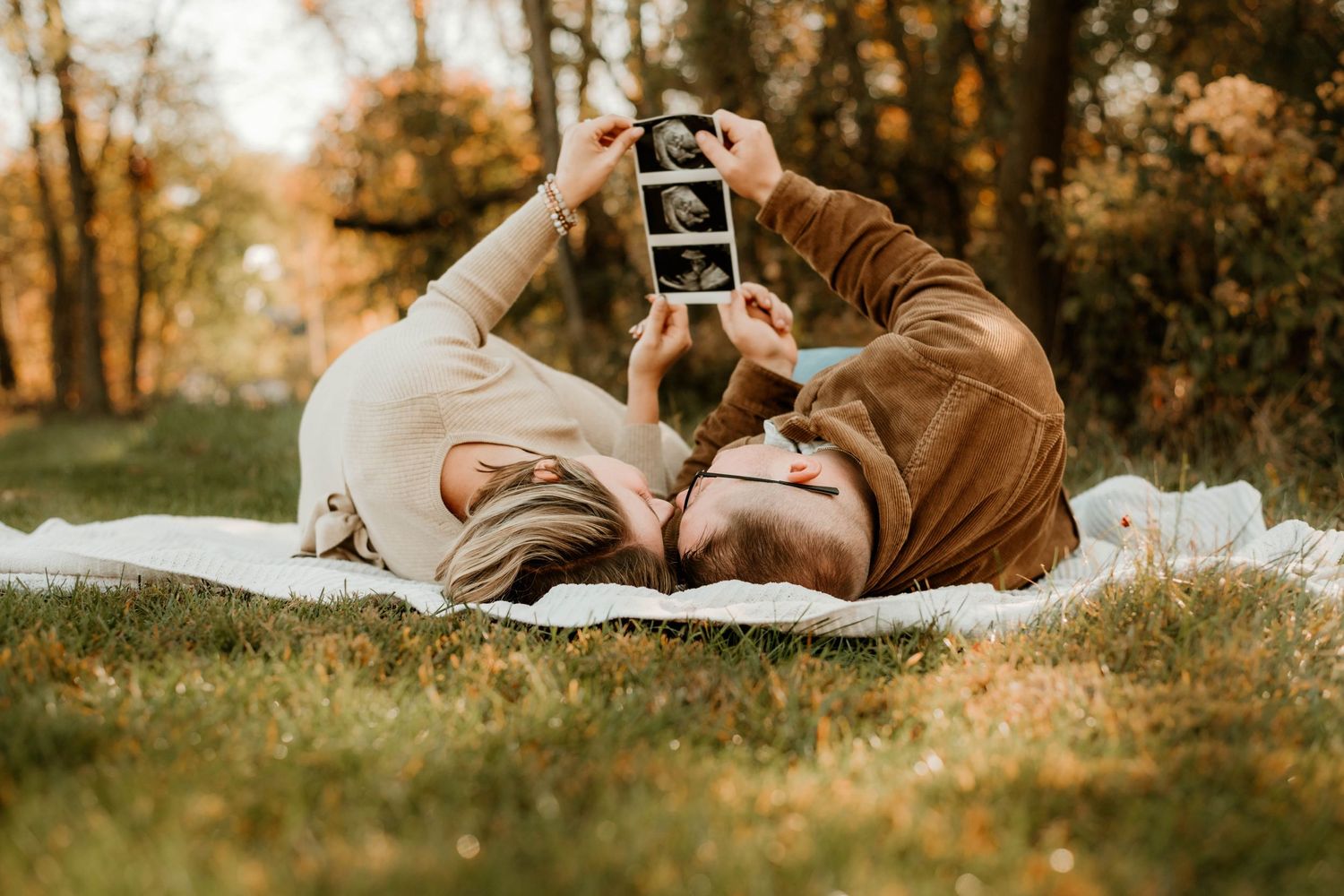 Person lying on blanket in grass holding sonogram during golden hour.