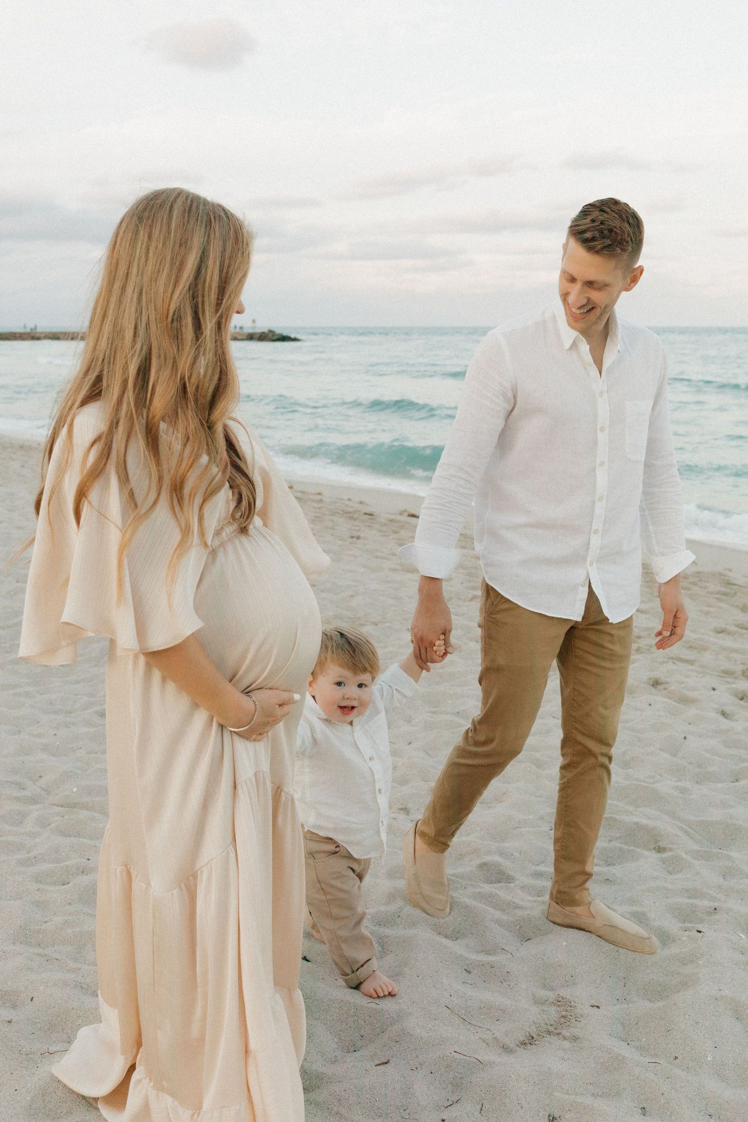 A family enjoys a moment together on a beach with turquoise waters and cloudy skies in the background.