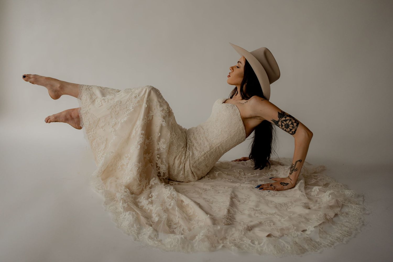 Person in vintage-style dress and hat poses dramatically on white background.