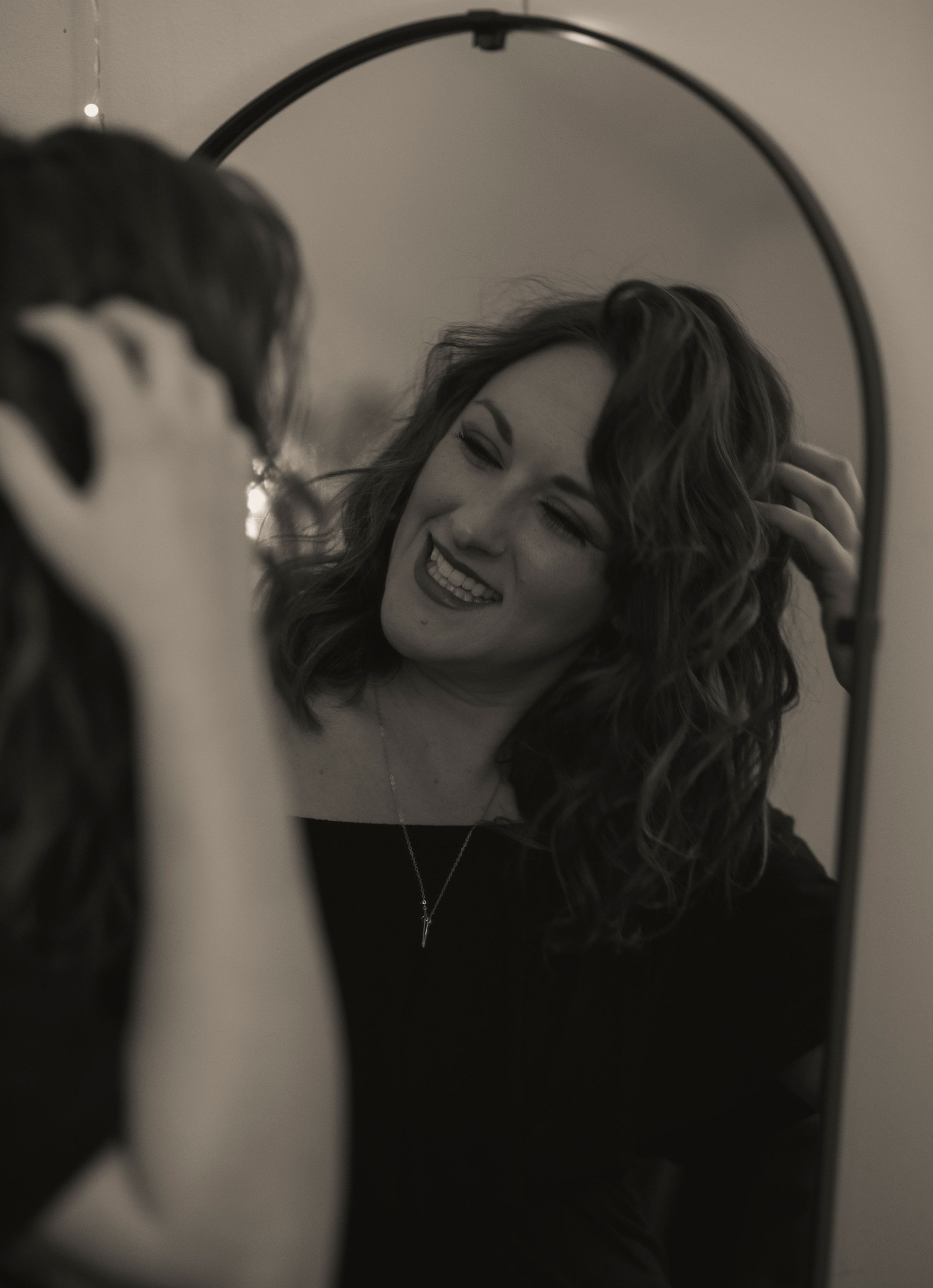 Artistic black and white mirror reflection shows woman with curly hair smiling.