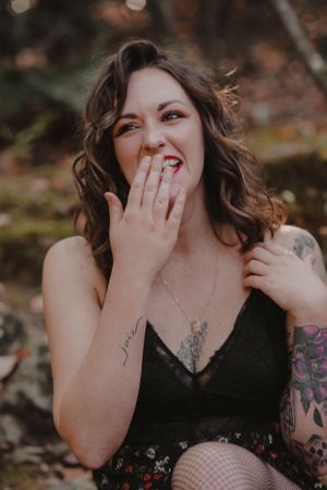 Playful portrait of a woman with tattoos laughing while covering her mouth.