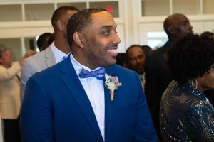 A groom in a sharp royal blue suit and polka dot bow tie smiles during his wedding ceremony.